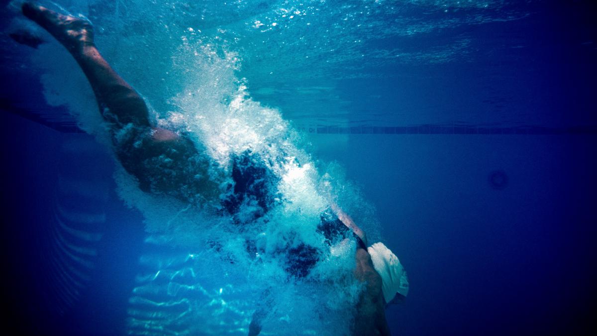 Underwater photo of a swimmer diving into a pool creating a splash against a blue background.