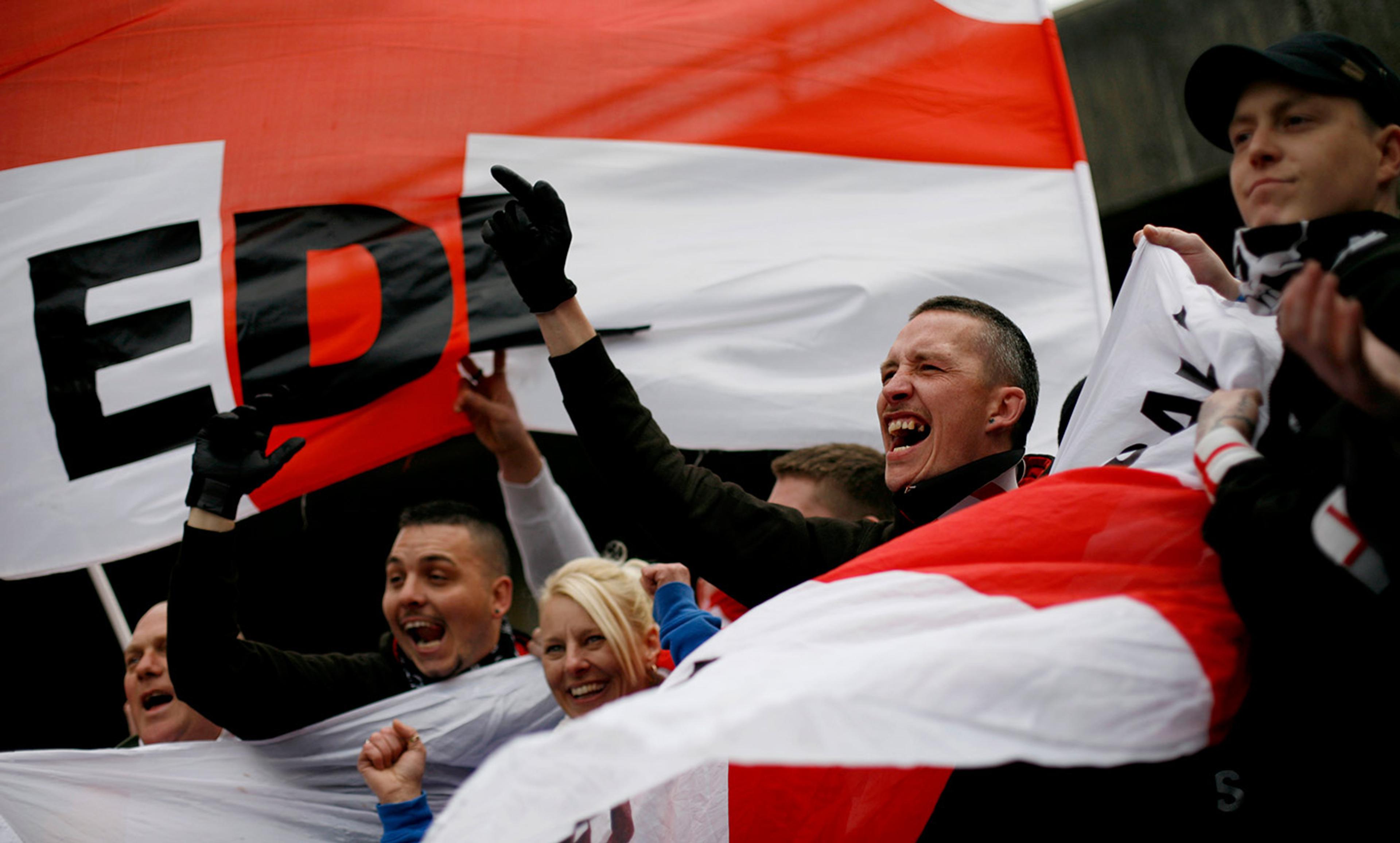 Photo of a group of people holding and waving red, white and black flags, some shouting.