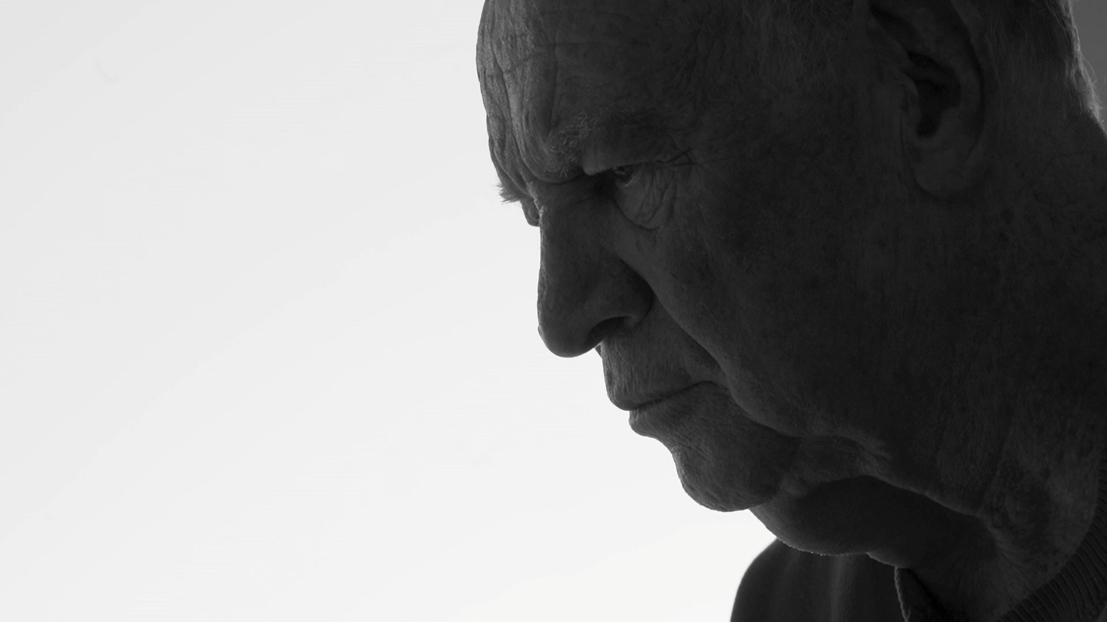 Black-and-white photo of elderly man’s profile, side lit with soft light against a white background.