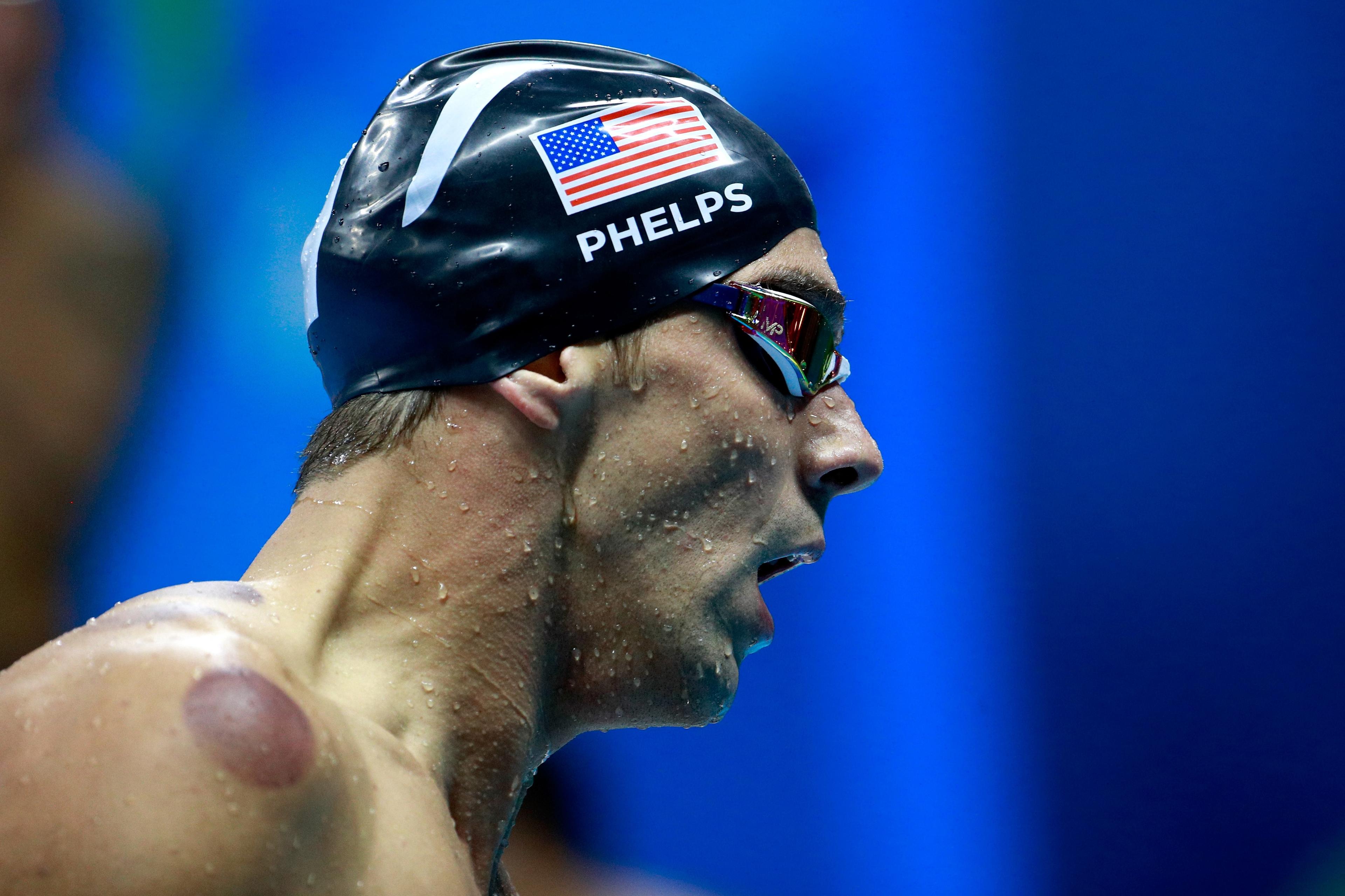 Photo of a swimmer with goggles and cap, water droplets visible on skin, seen in profile against a blue background.