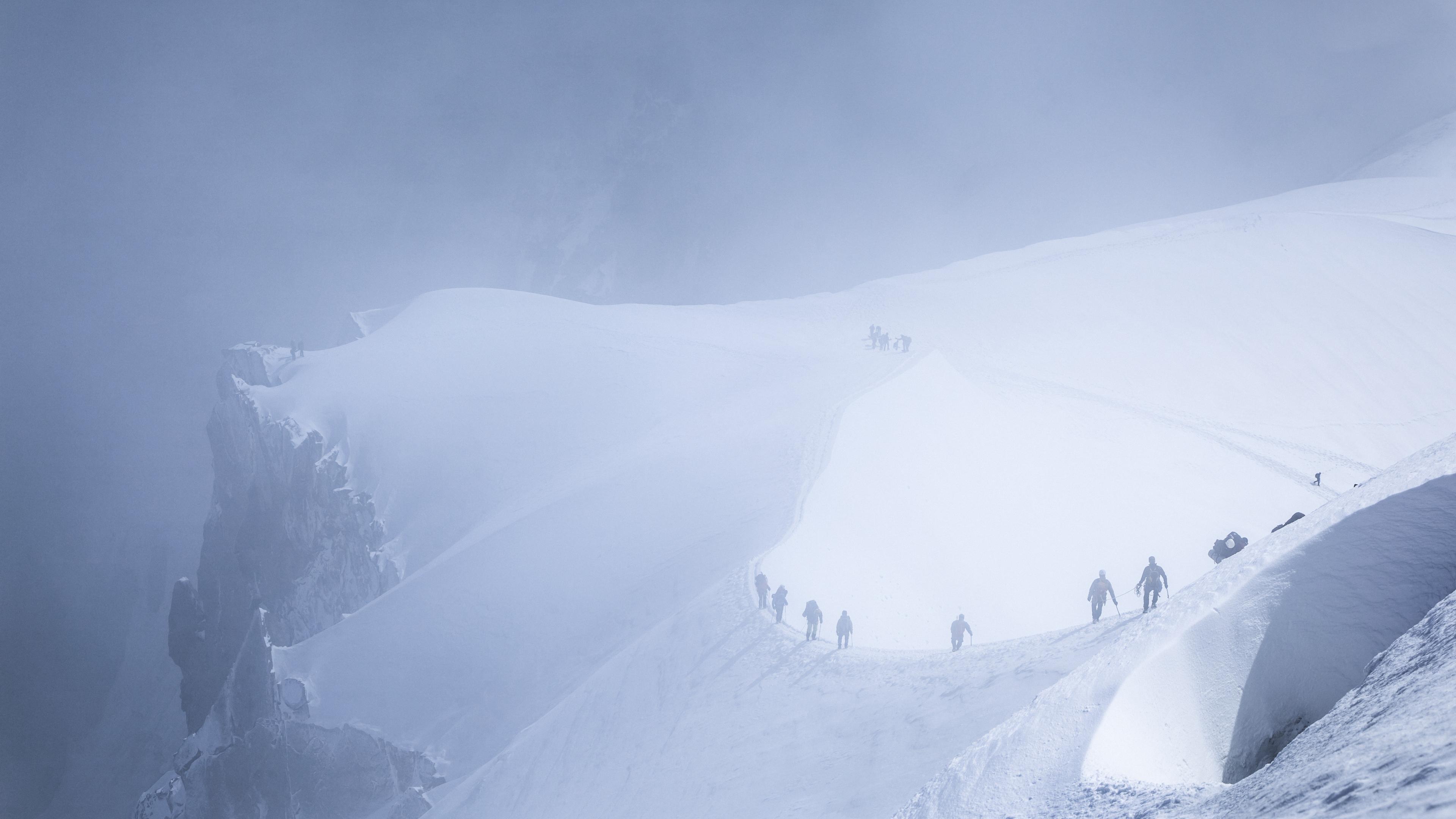Photo of climbers trekking on a snow-covered mountain ridge shrouded in mist and clouds.