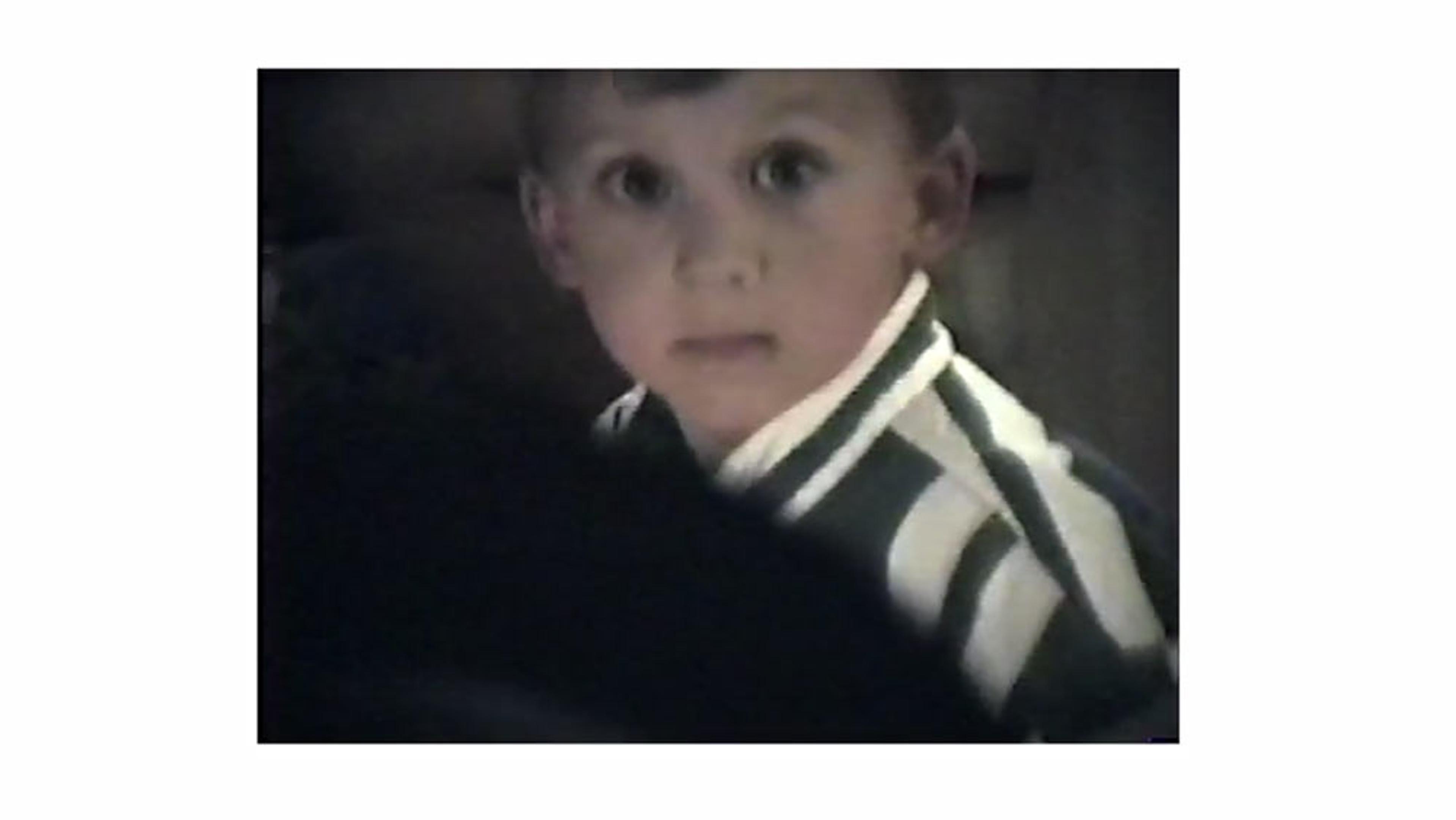 A young child with wide eyes wearing a striped shirt, looking at the camera in a dimly lit room.