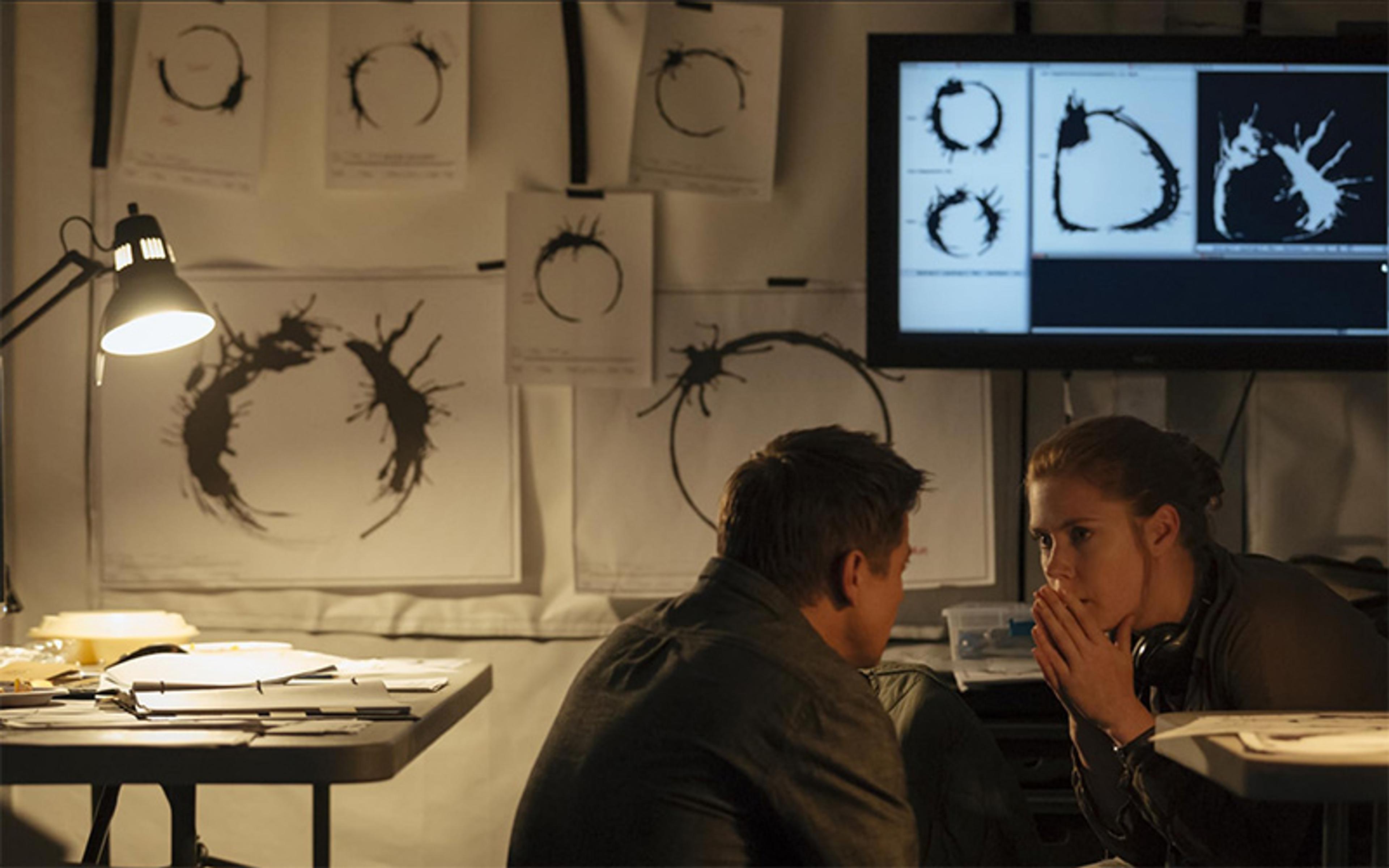 A man and a woman discussing in a room with alien circle symbols on paper on the walls and a computer screen.