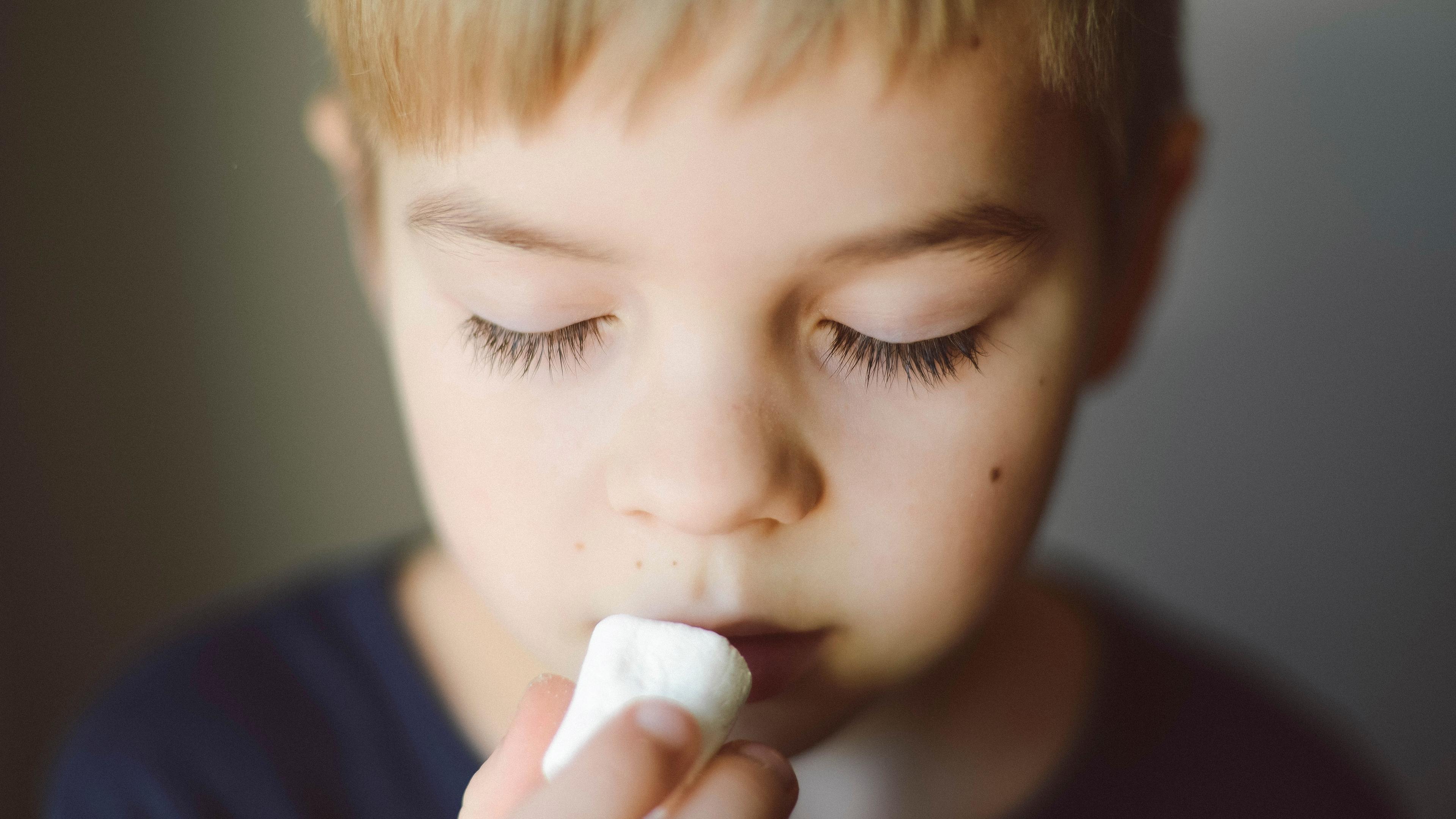 Photo of a young child holding a marshmallow close to their mouth eyes closed in contemplation.