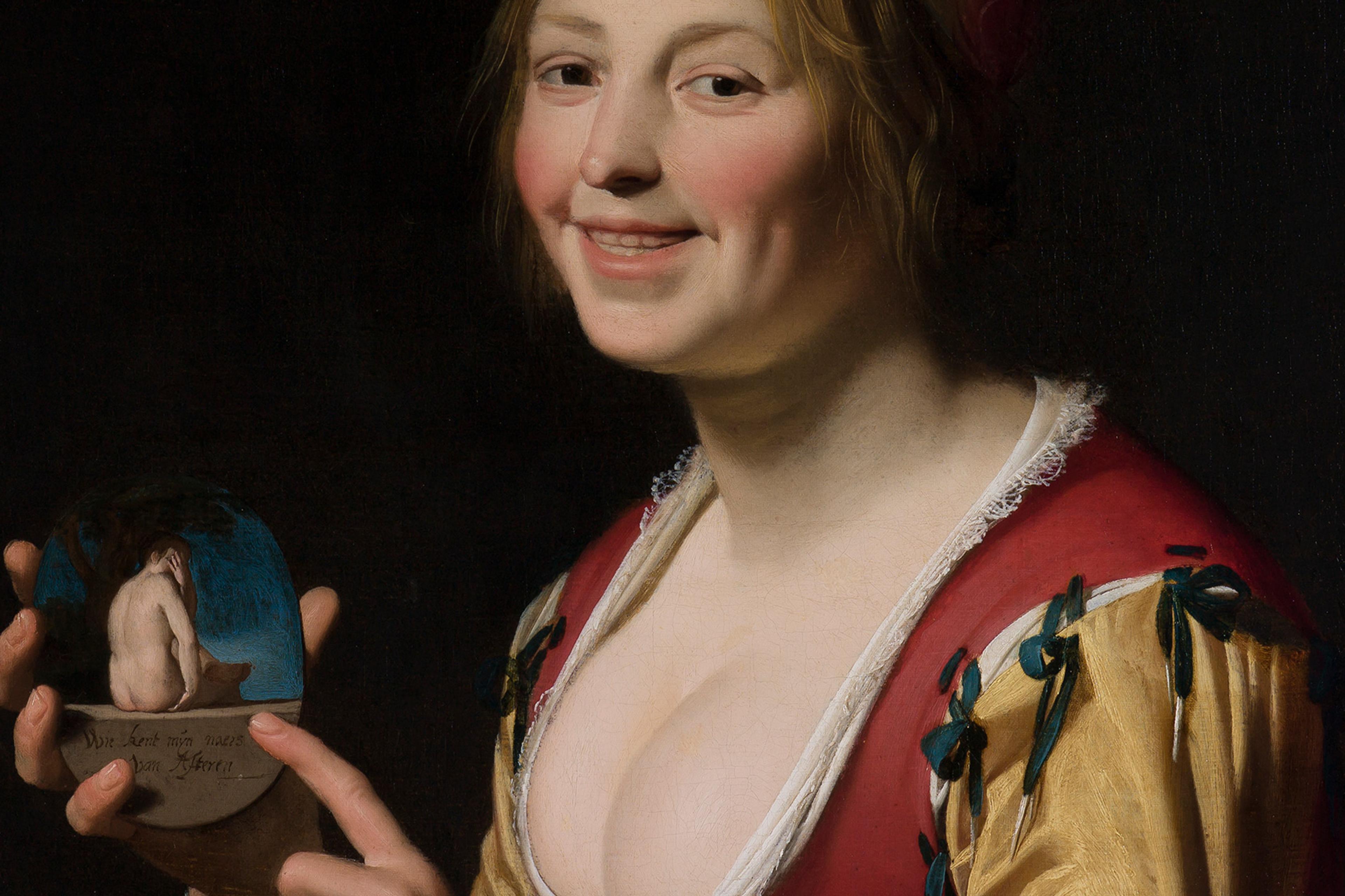 A woman in period dress smiles while holding a small object depicting a nude seated figure.