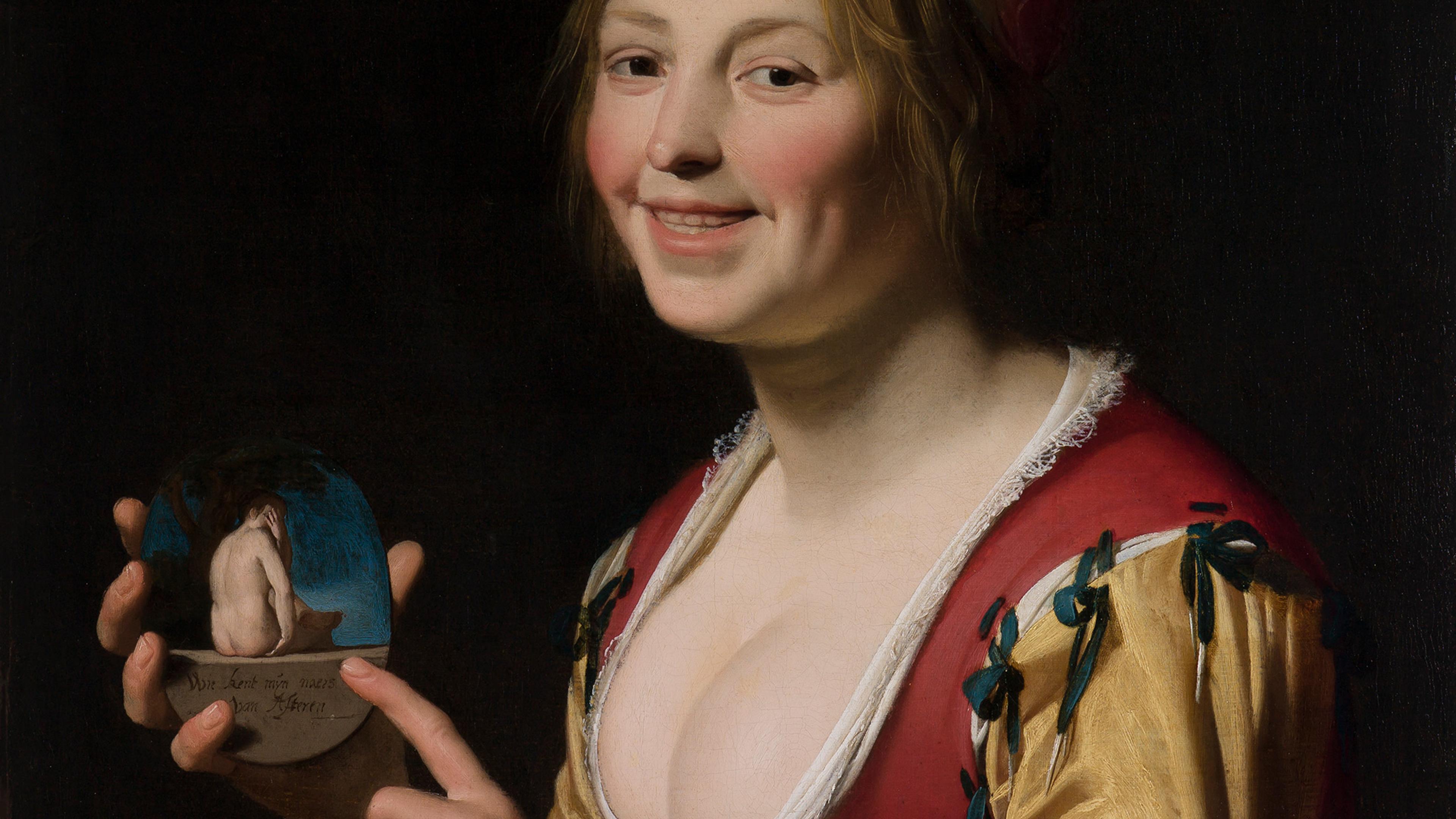 A woman in period dress smiles while holding a small object depicting a nude seated figure.
