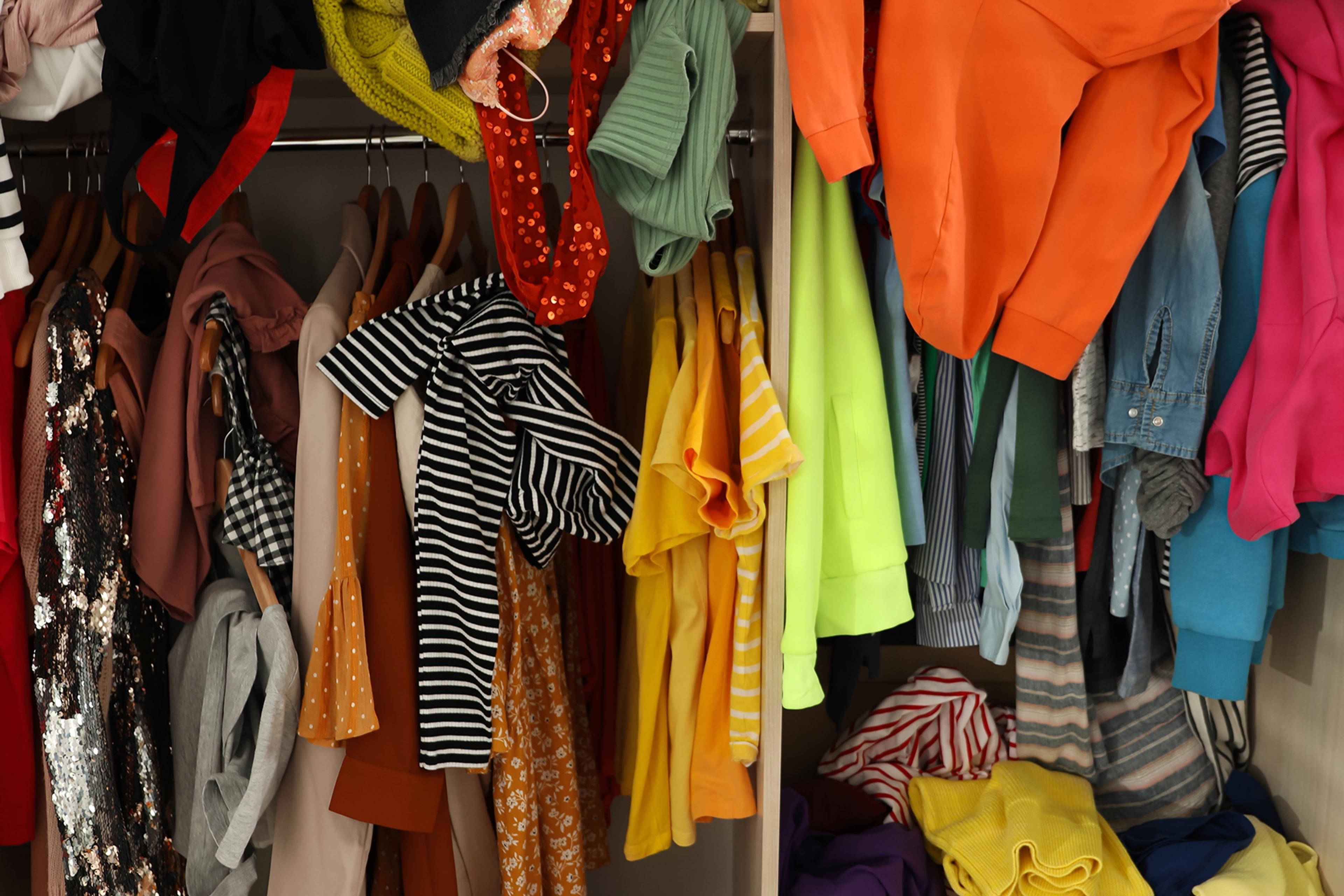 Photo of a messy wardrobe with mixed colourful clothes on hangers and shelves, showing disorganisation and variety in styles.
