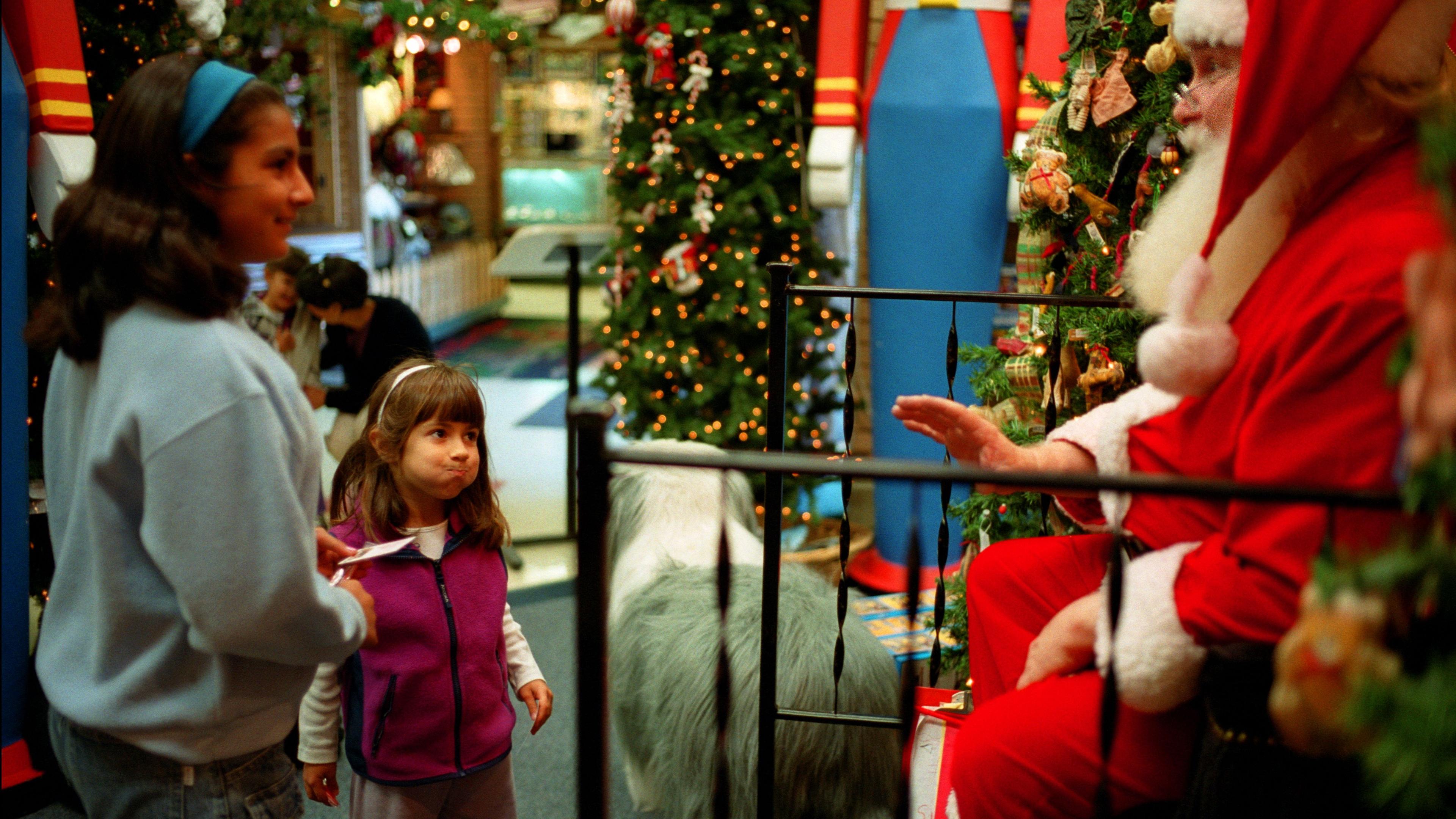 Photo of two children visiting Santa Claus in a festive setting with Christmas trees and decorations.