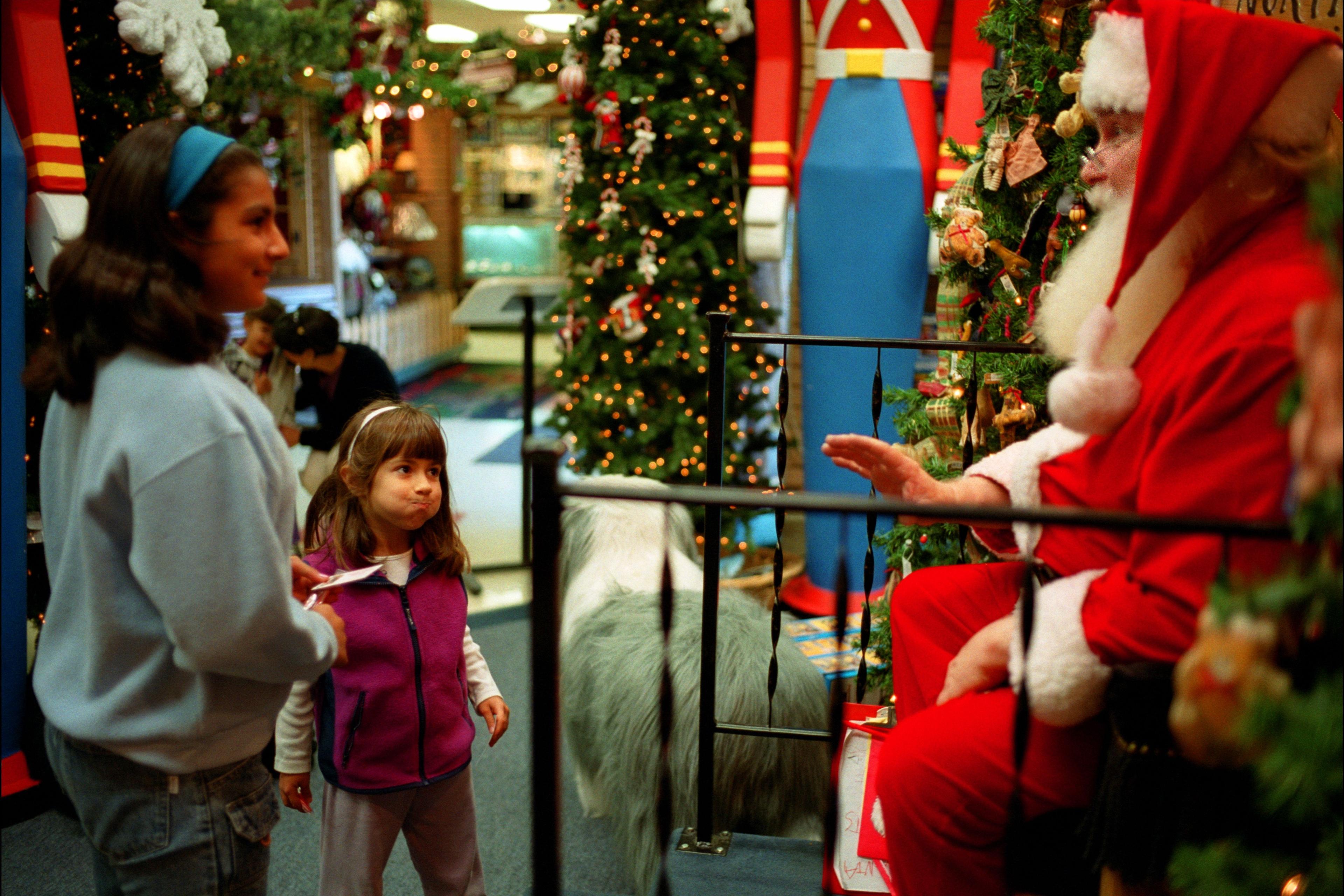 Photo of two children visiting Santa Claus in a festive setting with Christmas trees and decorations.