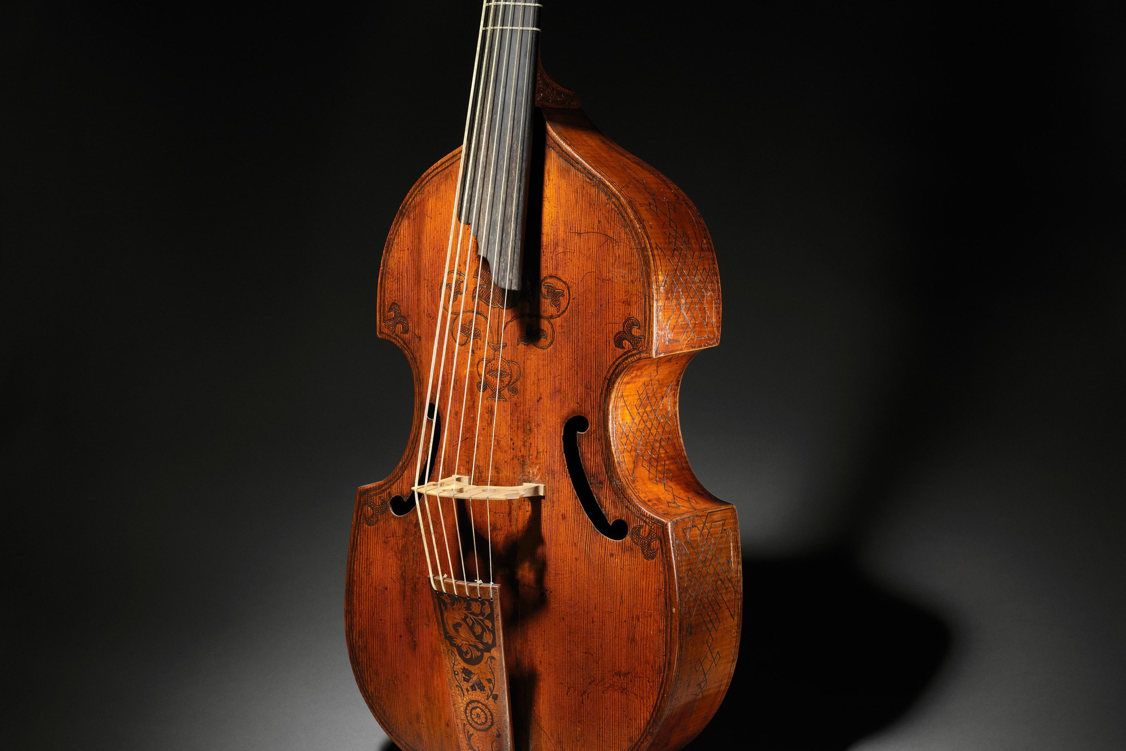 An antique string instrument with intricate carvings on a dark background.