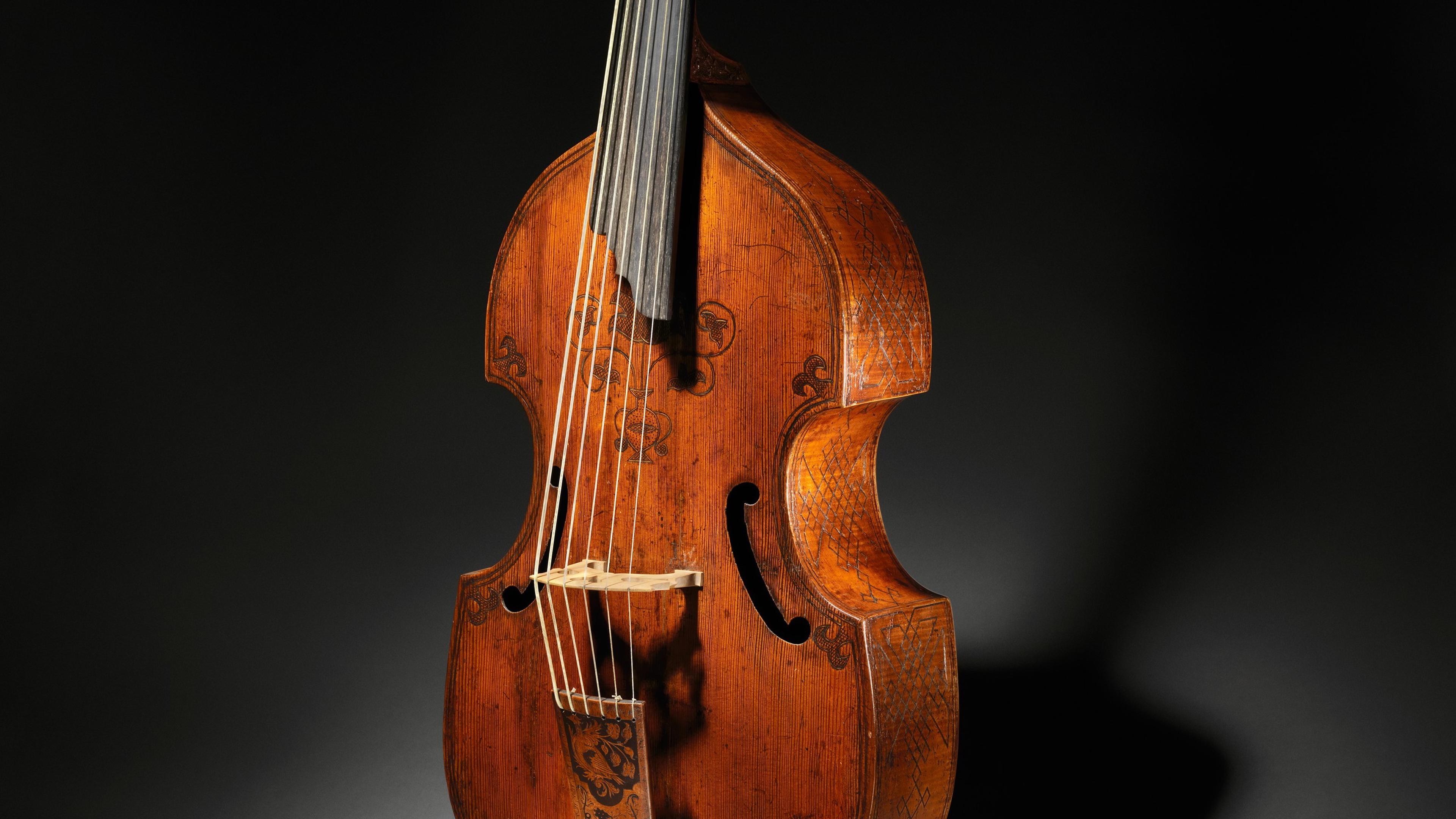 An antique string instrument with intricate carvings on a dark background.