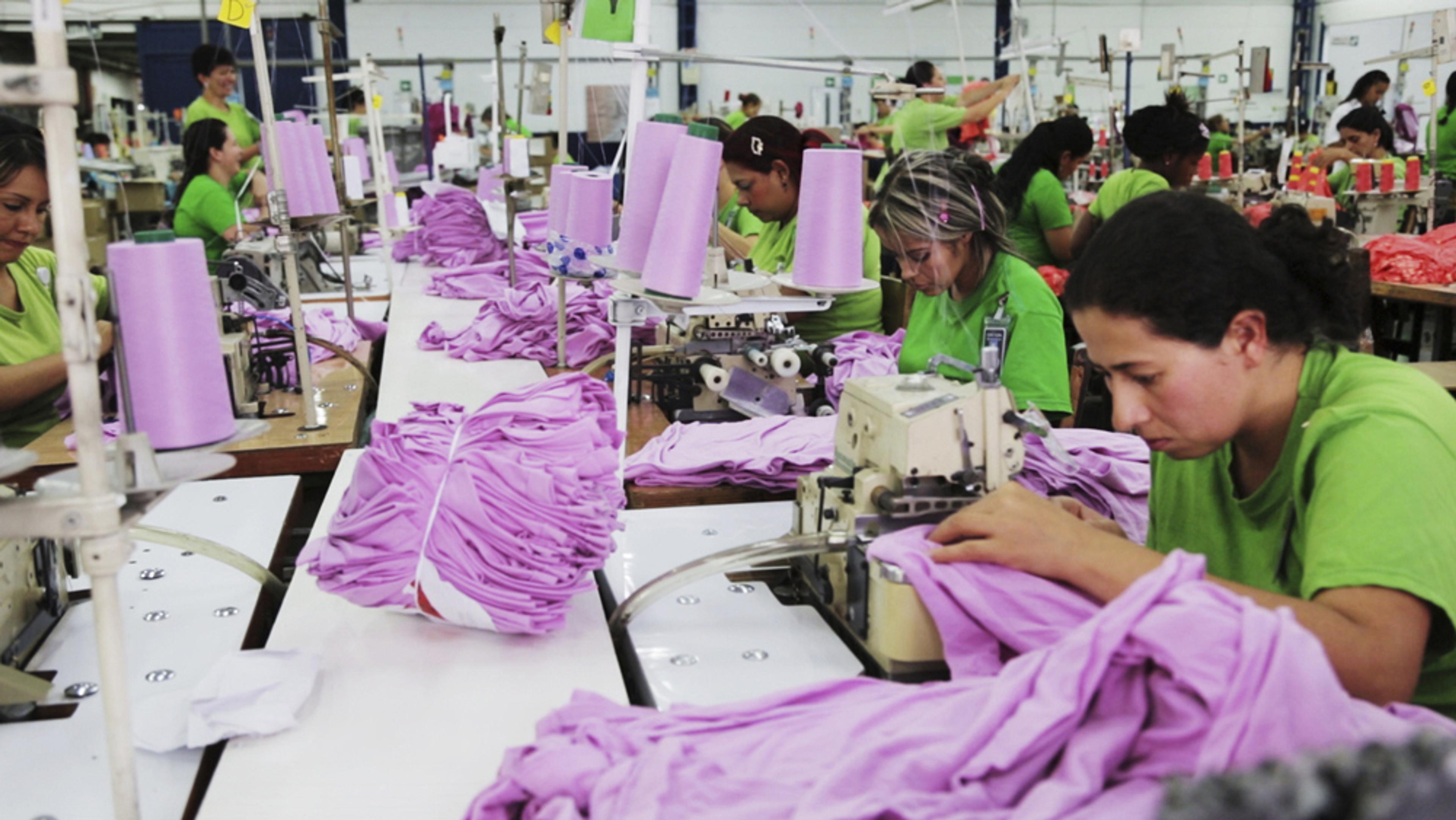 Workers in green shirts operating sewing machines, stitching purple fabric in a garment factory, focused on their tasks.