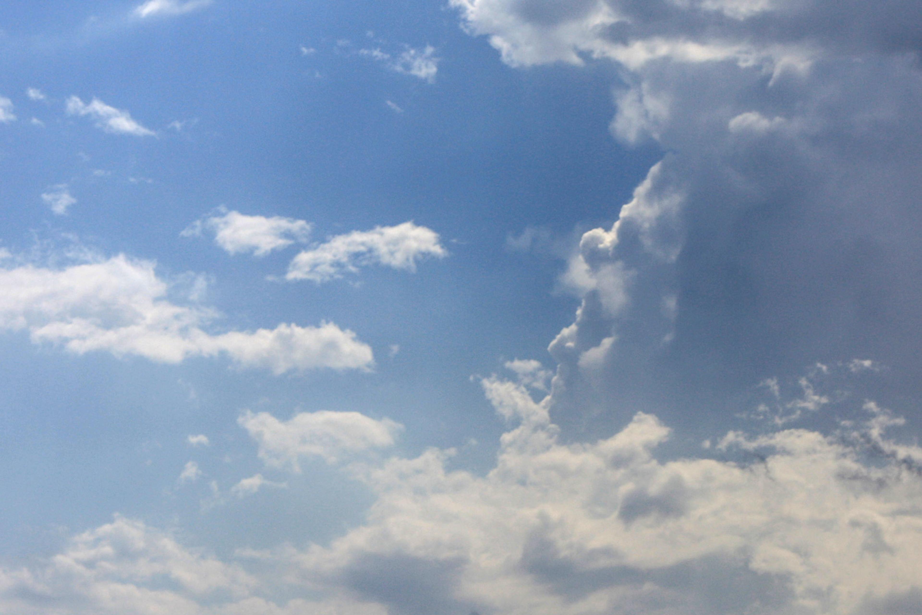 Photo of a blue sky with scattered white clouds and larger clouds forming on one side.