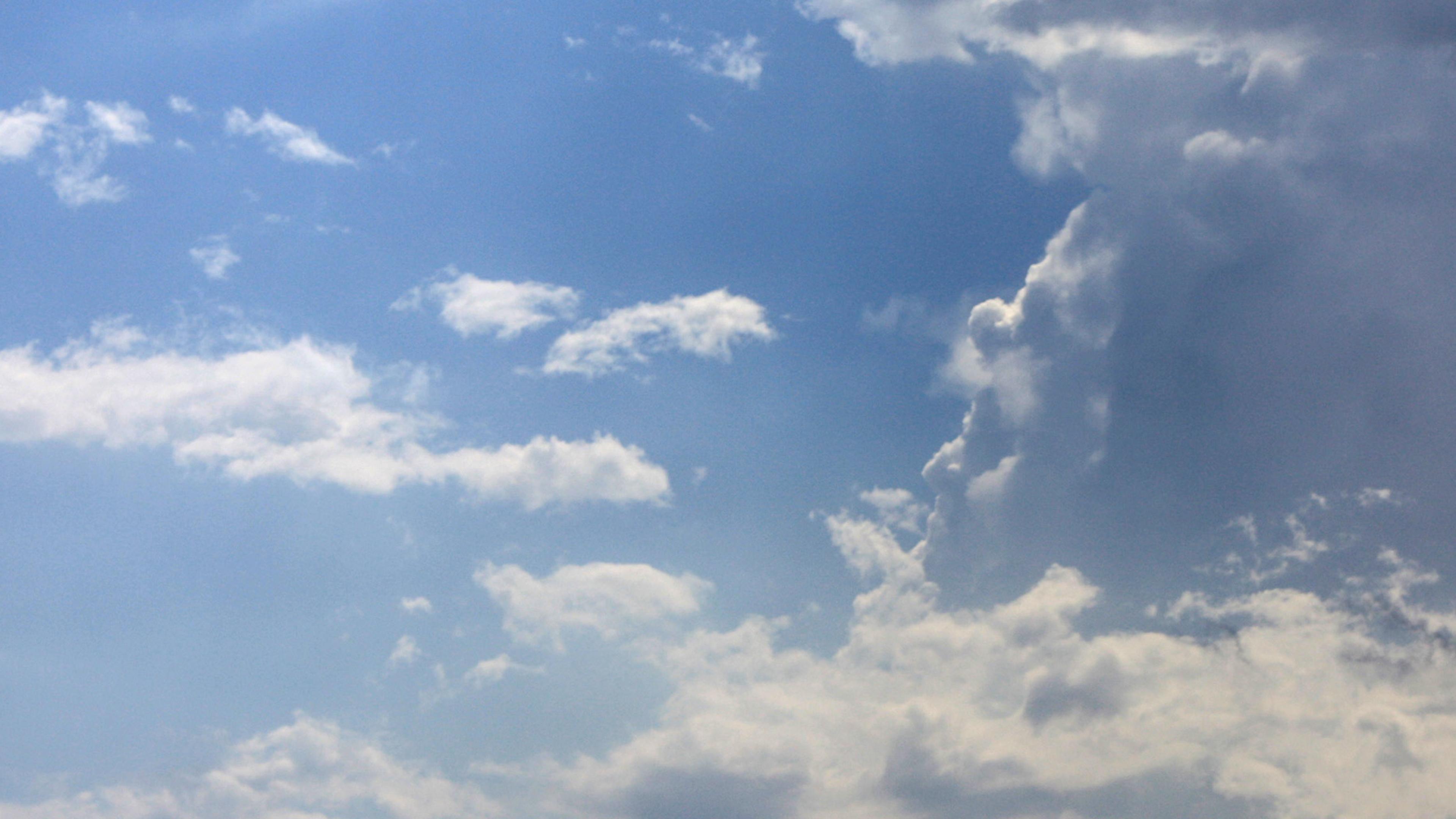 Photo of a blue sky with scattered white clouds and larger clouds forming on one side.