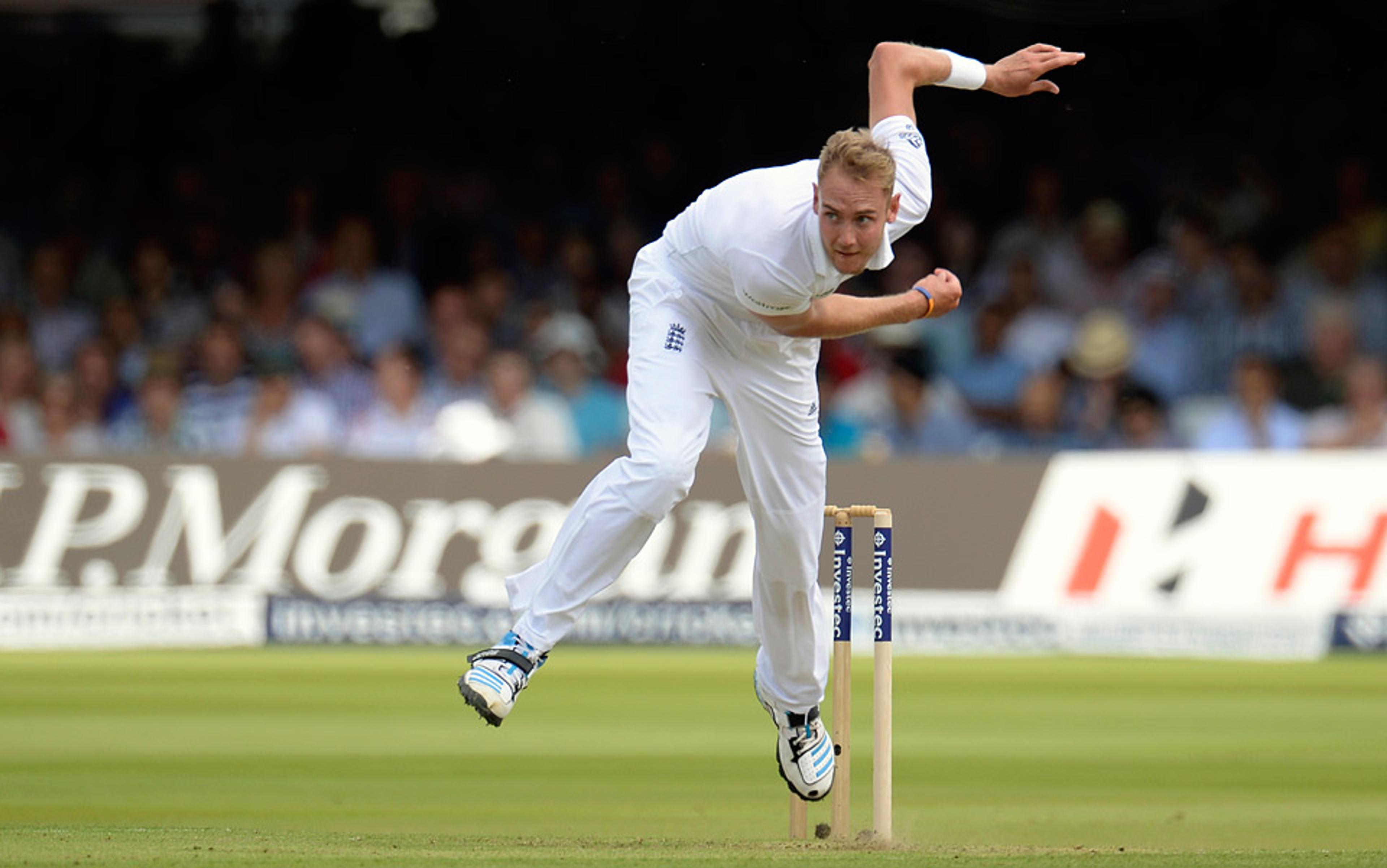 A cricket player in white uniform bowling during a match, with stumps in the background and audience watching attentively.