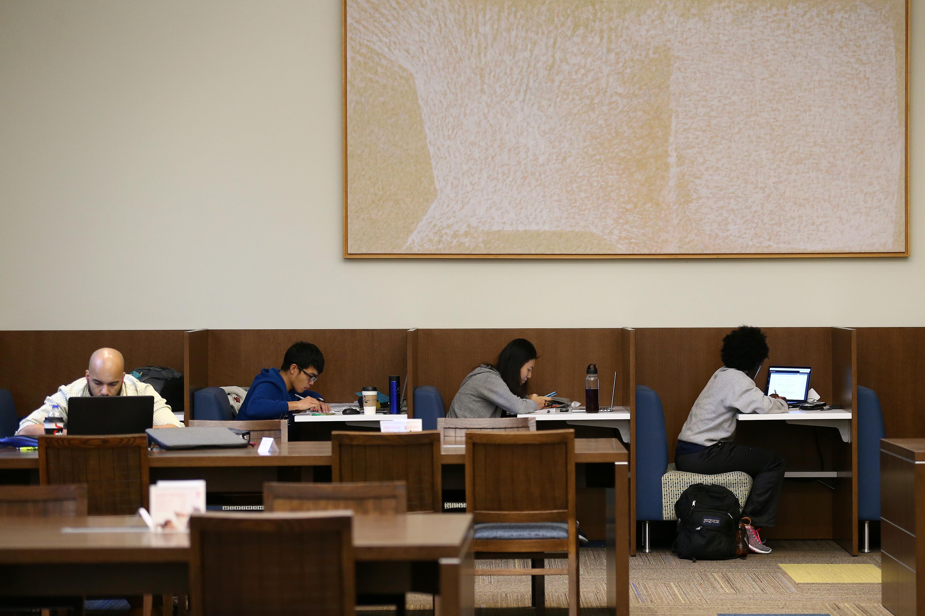 Photo of people studying at desks in a library with a large abstract painting on the wall above them.
