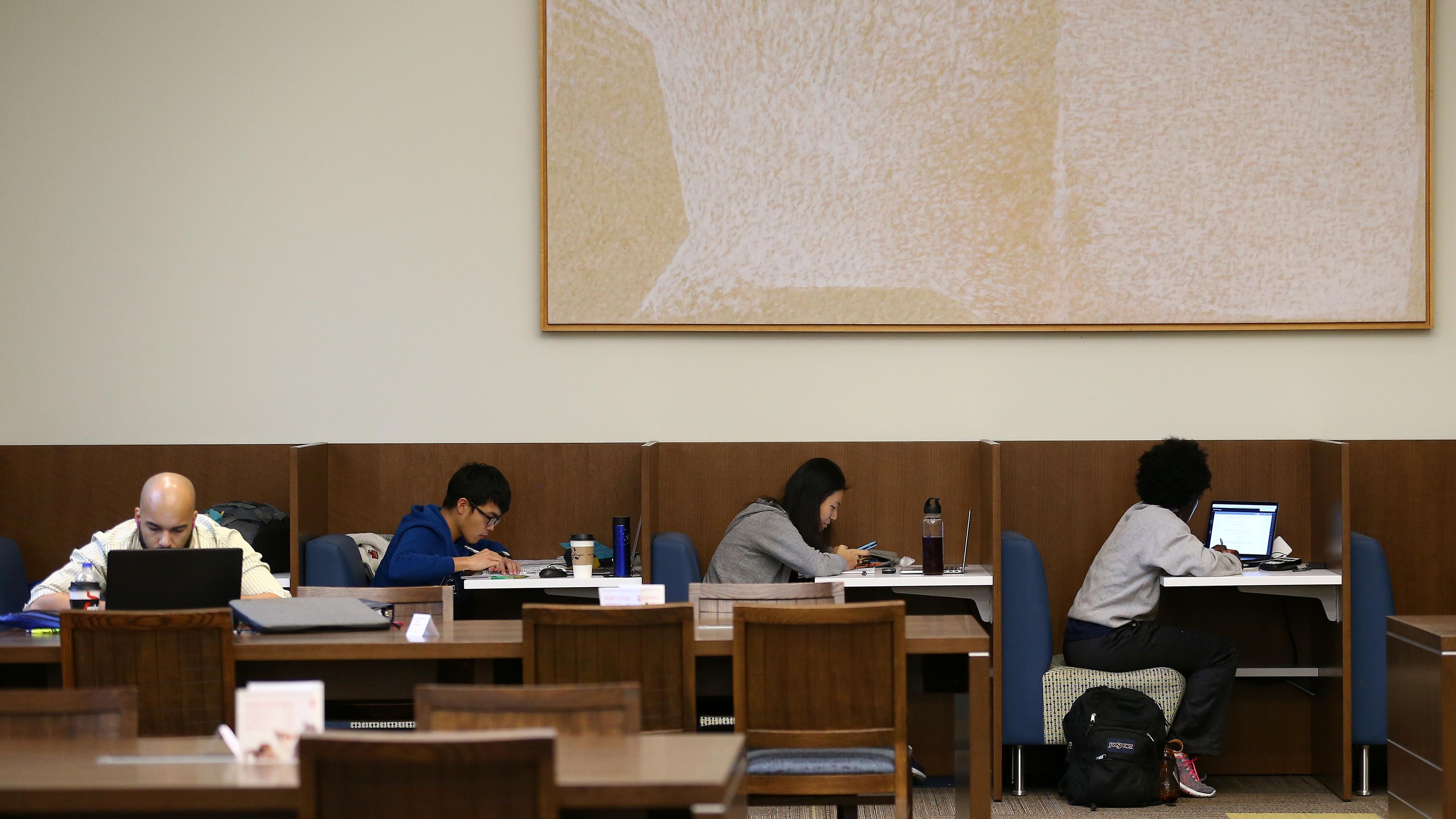 Photo of people studying at desks in a library with a large abstract painting on the wall above them.