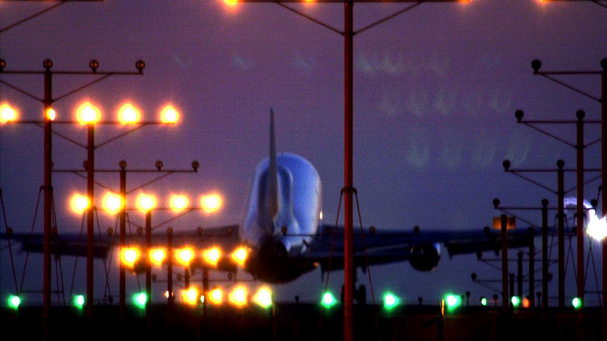 An aeroplane landing at dusk with runway lights glowing, surrounded by a purple sky and silhouetted light poles.