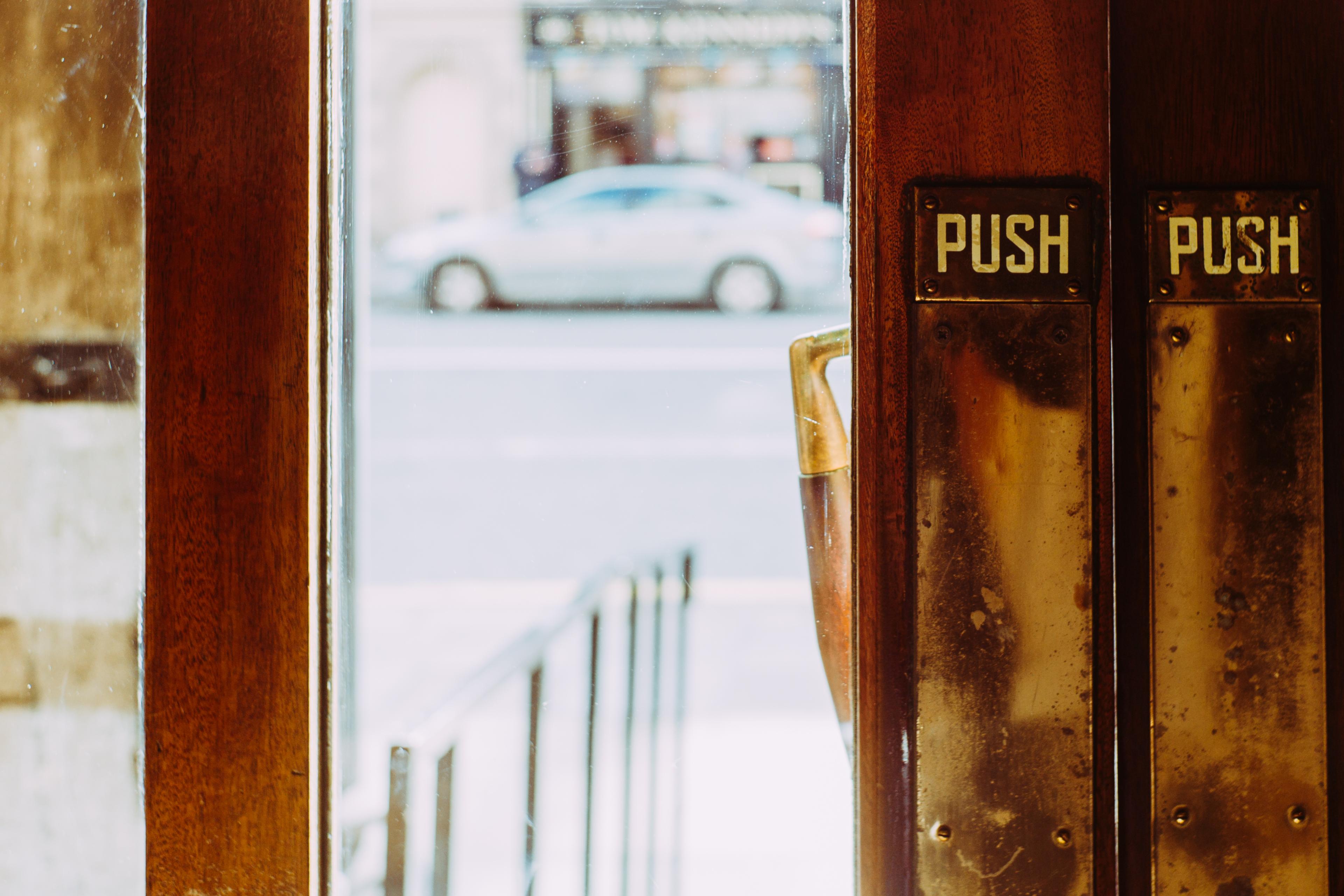 Photo of glass doors with push handles leading outside. A blurred car is visible through the doors.