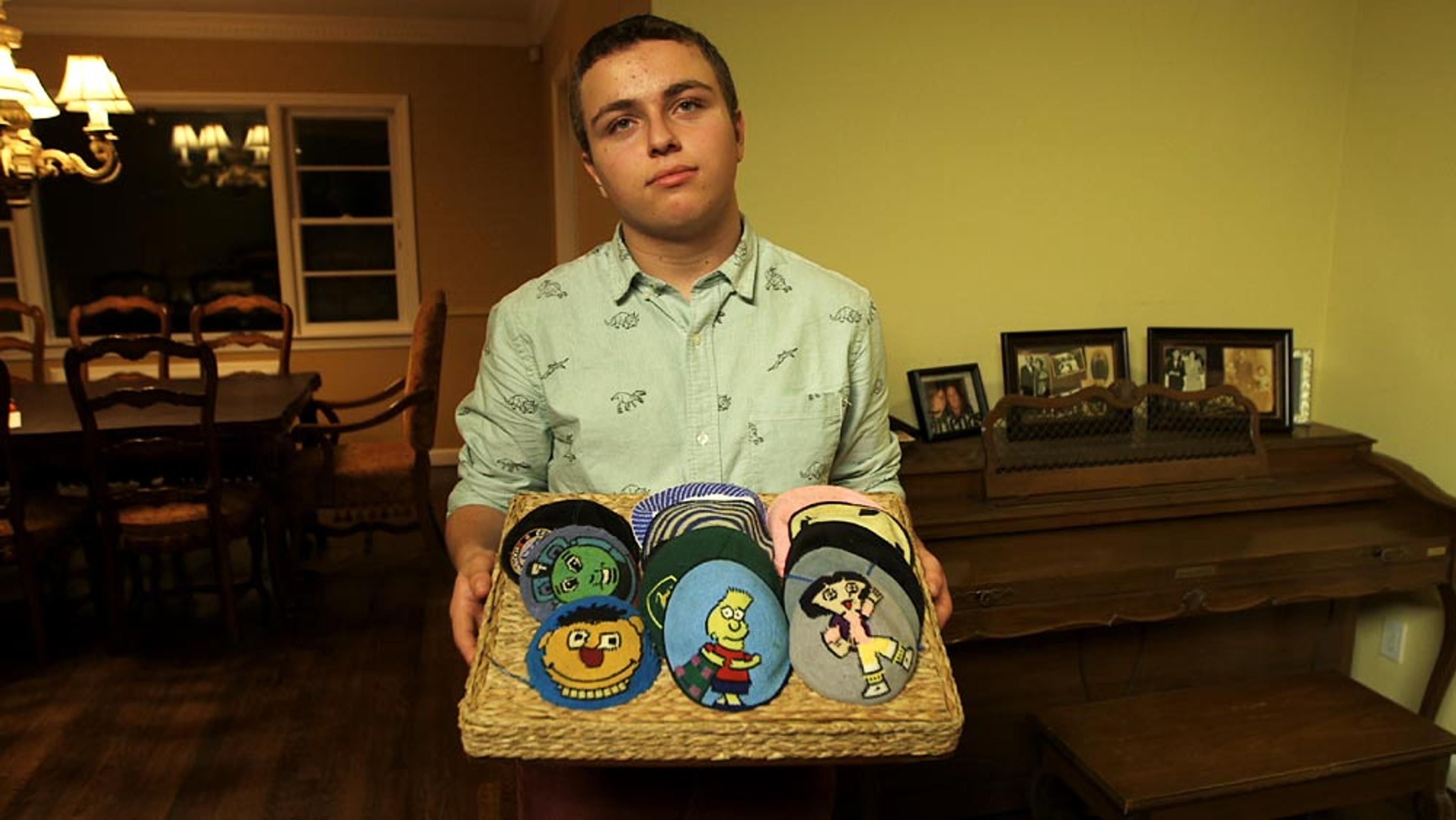 A young person holding a basket of colourful knitted skullcaps featuring cartoon characters, standing in a dining room with a piano.
