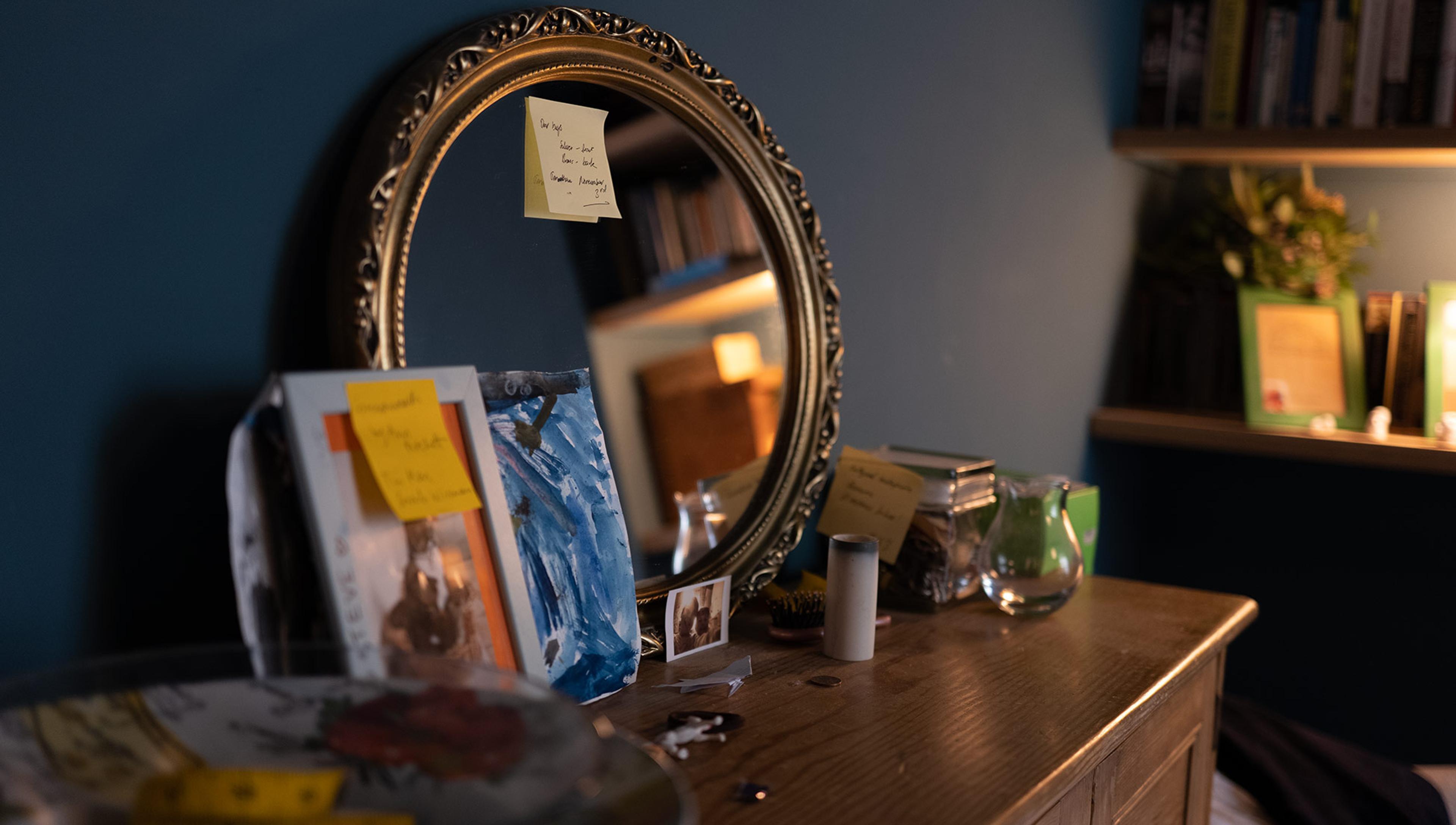 Sticky reminder notes are seen on a mirror and on various other items on top of a chest of drawers