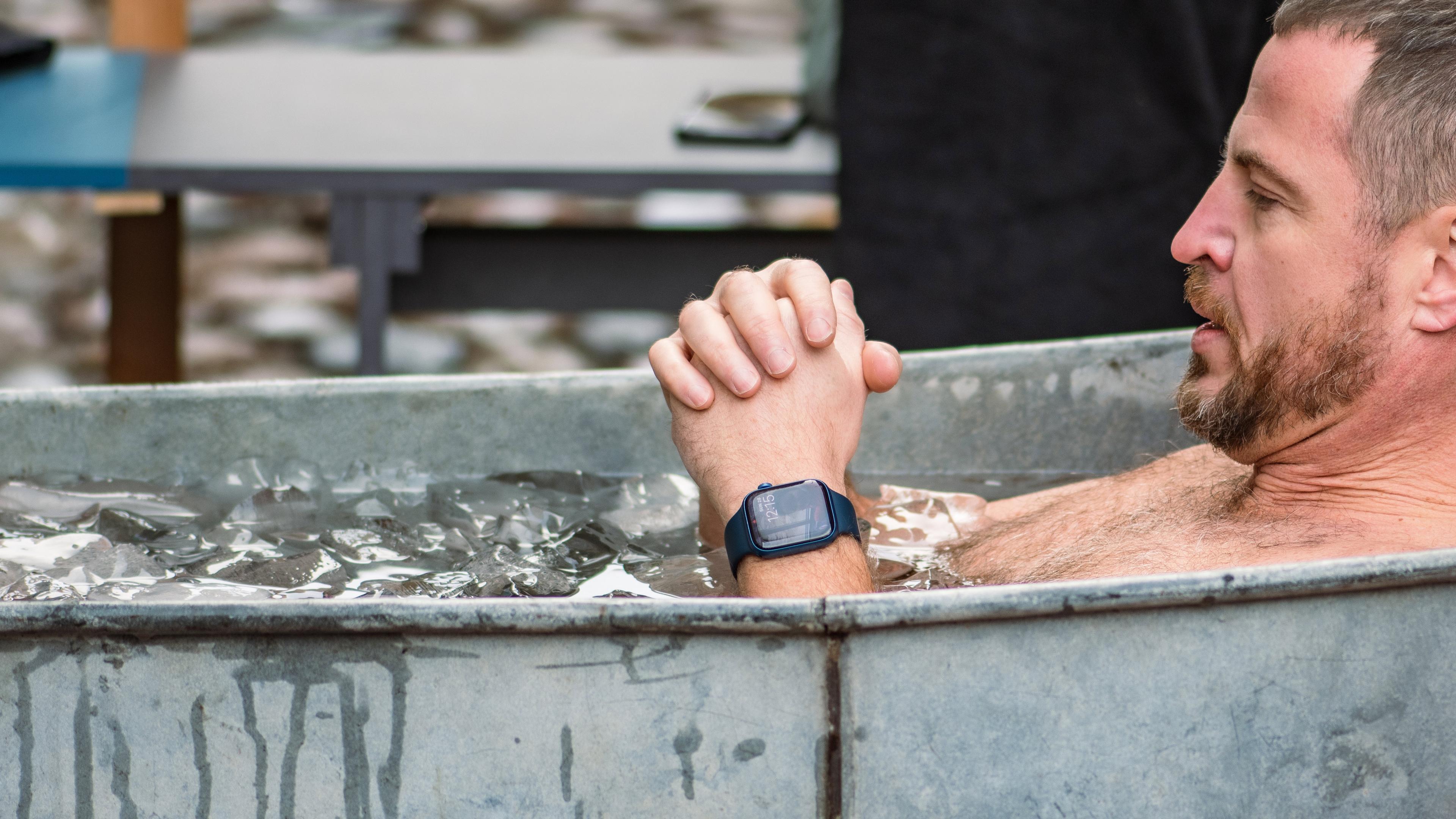 A man in an outdoor ice bath, clasping his hands and wearing a smartwatch.