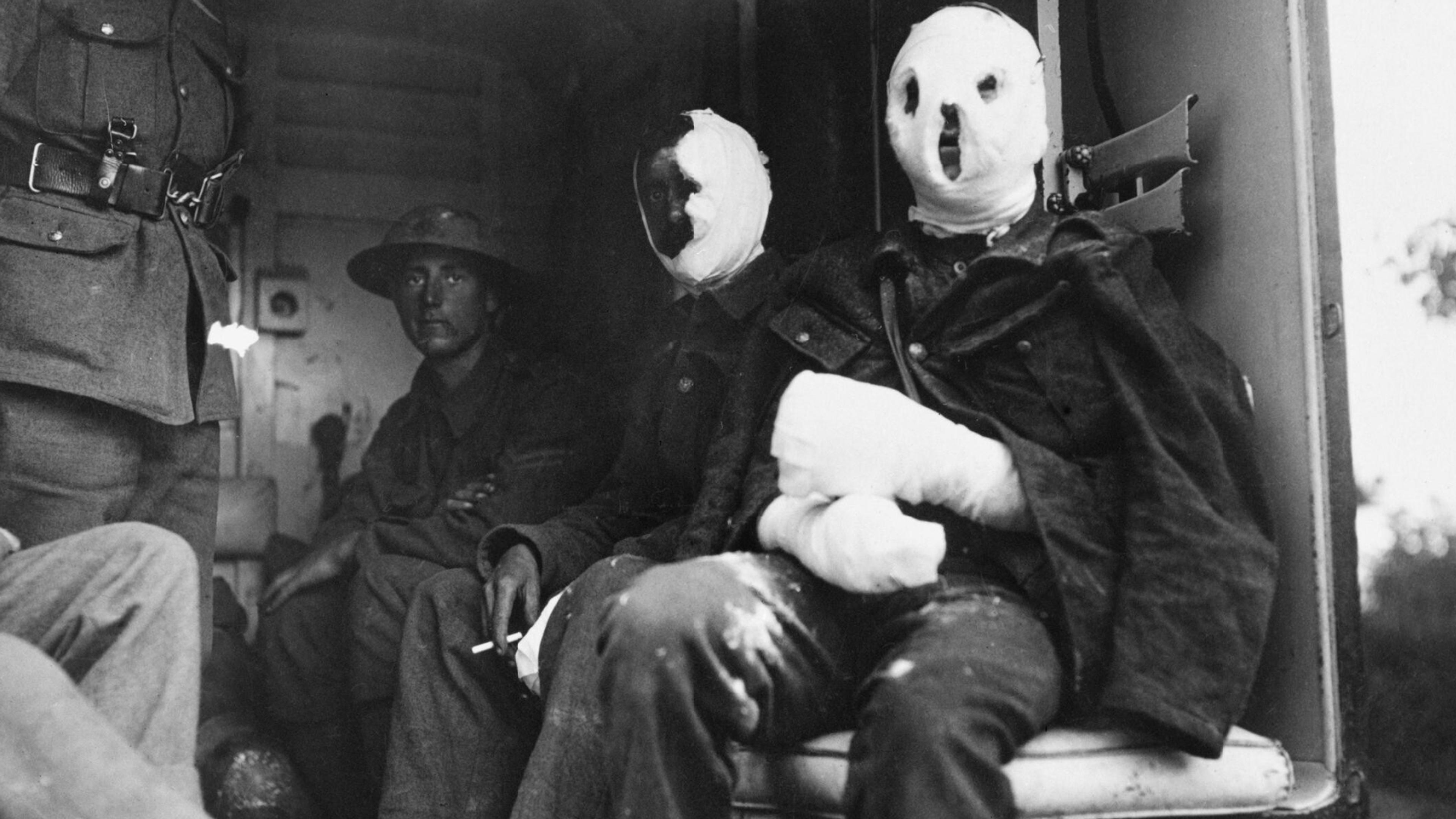 Black and white photo of soldiers in bandages sitting inside a vehicle during wartime, exhibiting visible injuries.