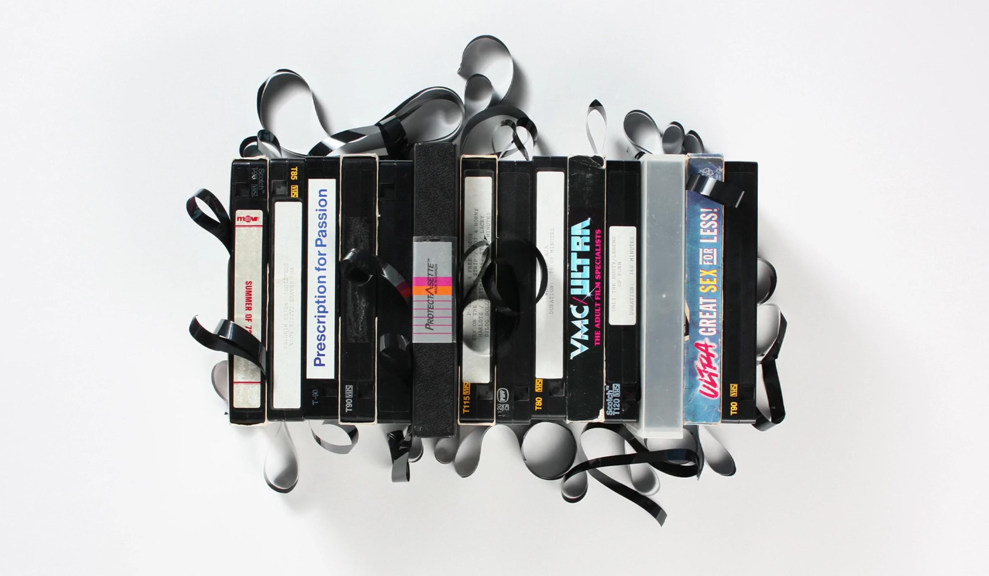 VHS tapes with loose, unwound tape ribbons scattered around, set against a plain white background.