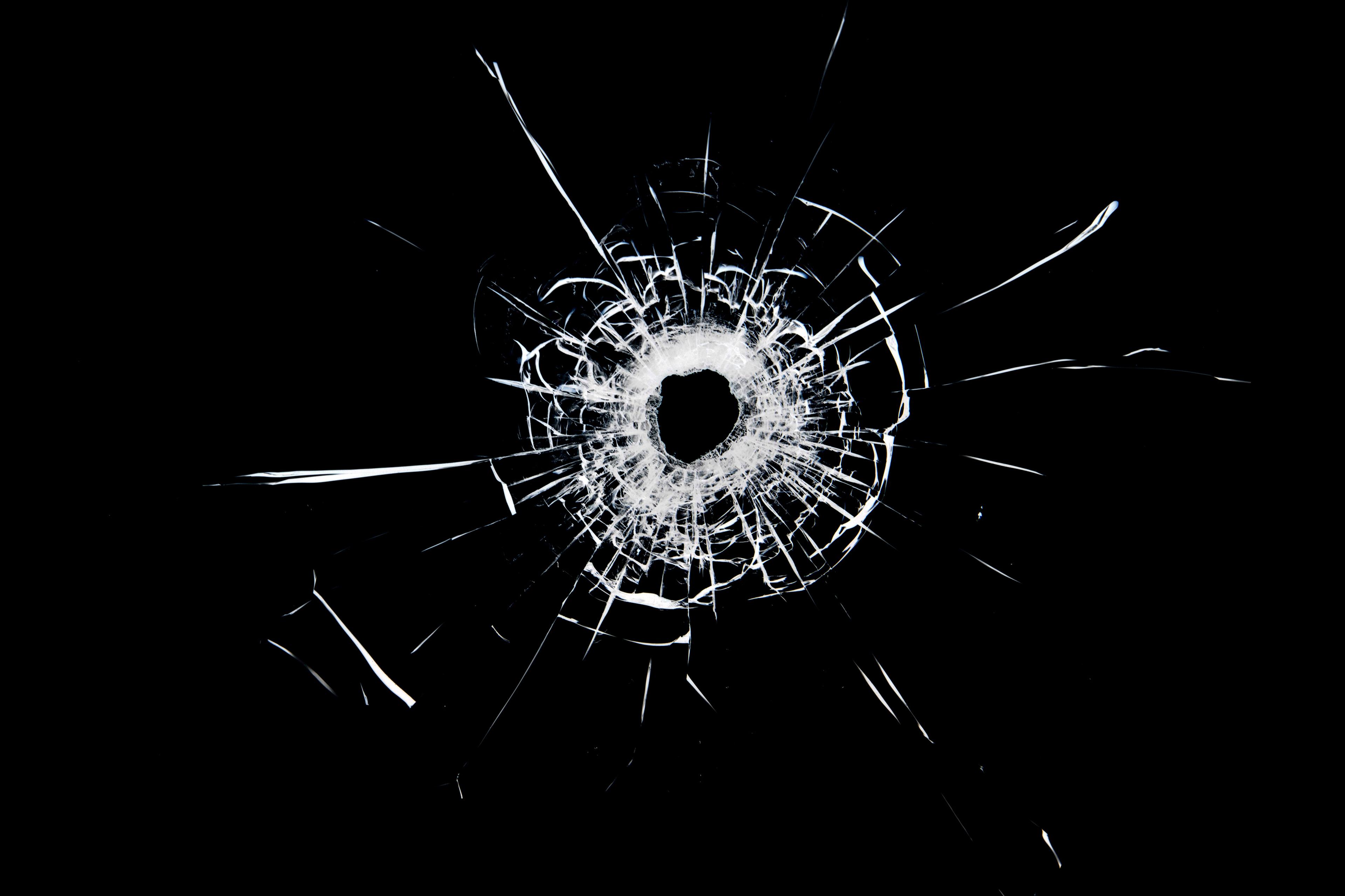 Photo of a bullet hole in glass, showing shattered glass patterns on a black background.