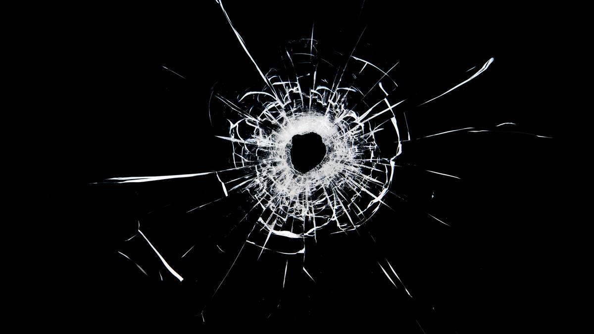 Photo of a bullet hole in glass, showing shattered glass patterns on a black background.