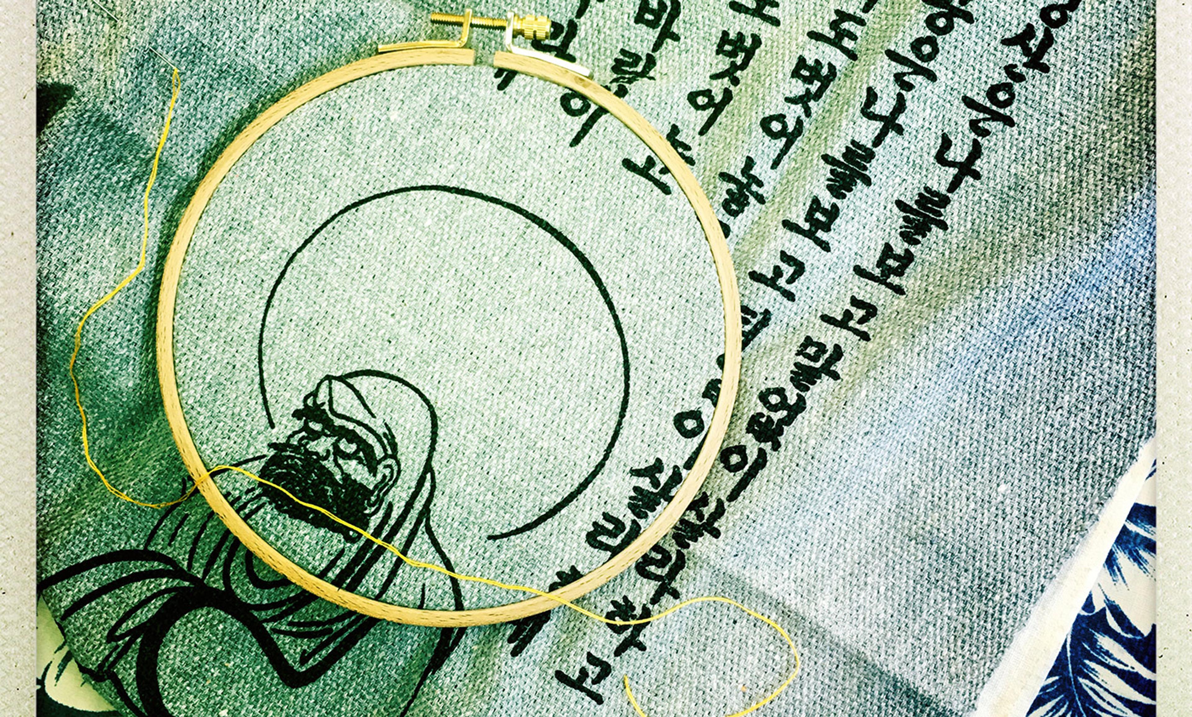 Embroidery fabric in a hoop with a black ink drawing of a bearded figure and surrounding text in a non-Latin script.