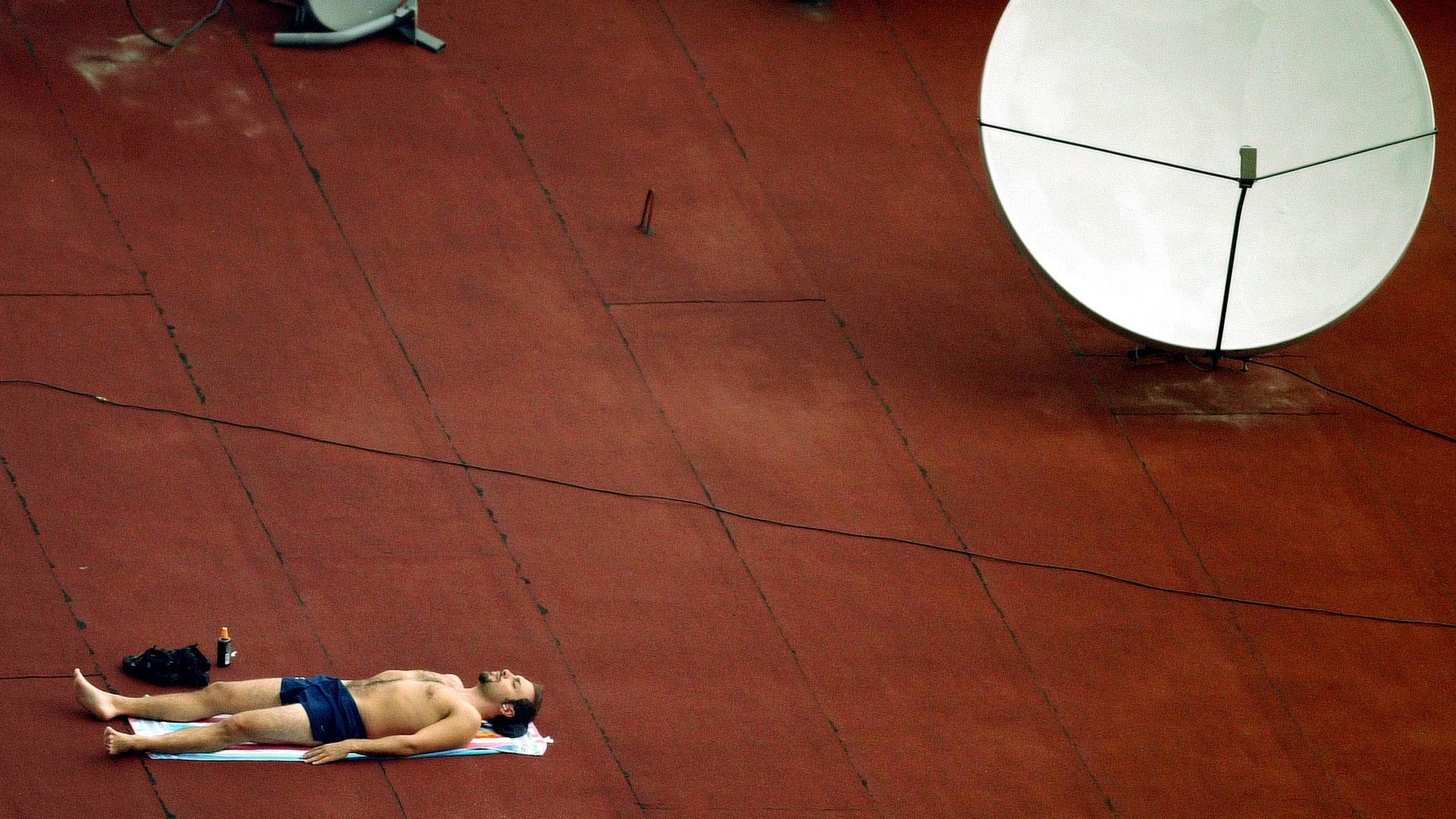 Photo of a man sunbathing on a rooftop next to a large satellite dish.