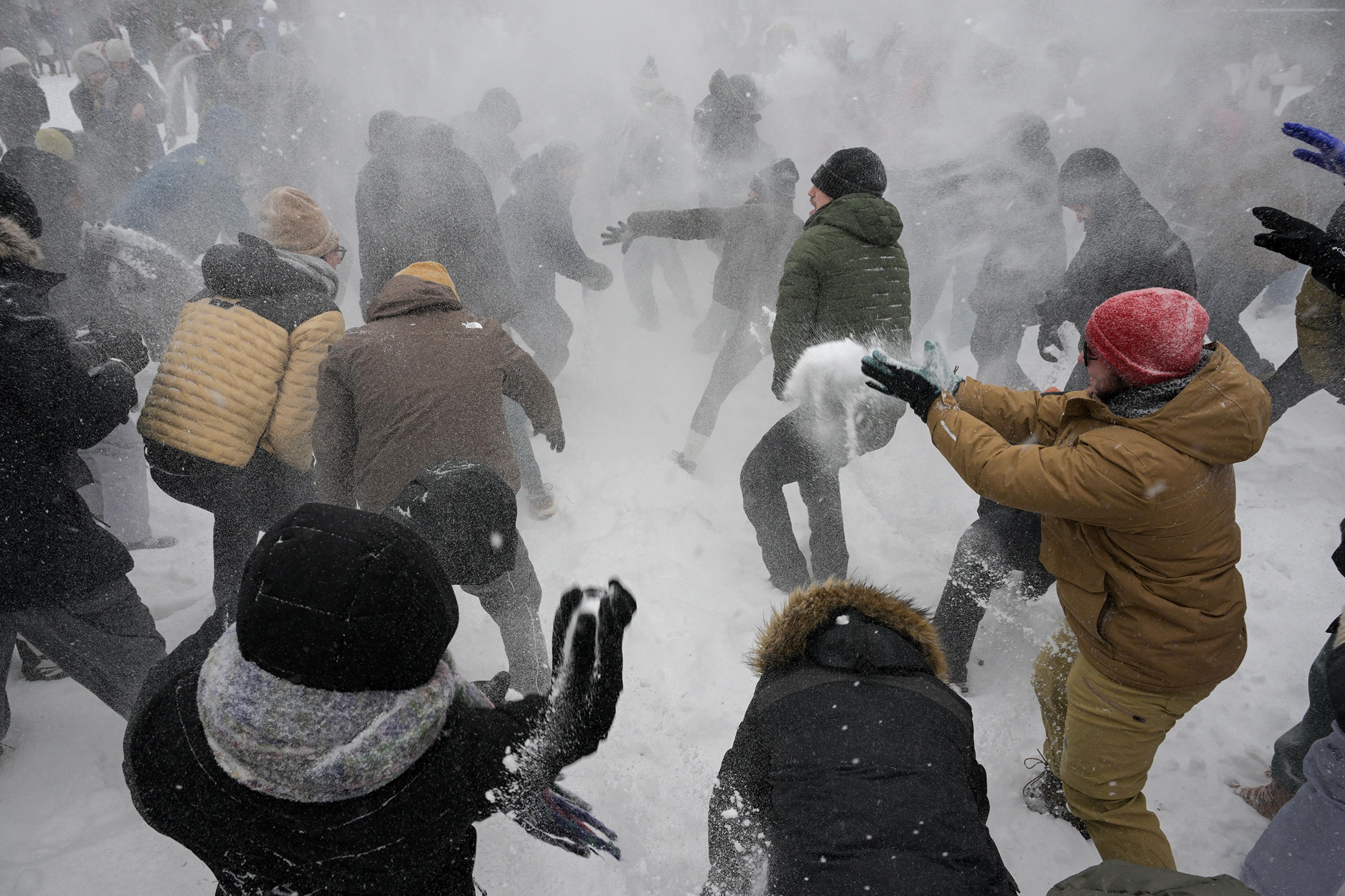 A lively snowball fight with people in winter clothing throwing snow outside amidst a snowy background.