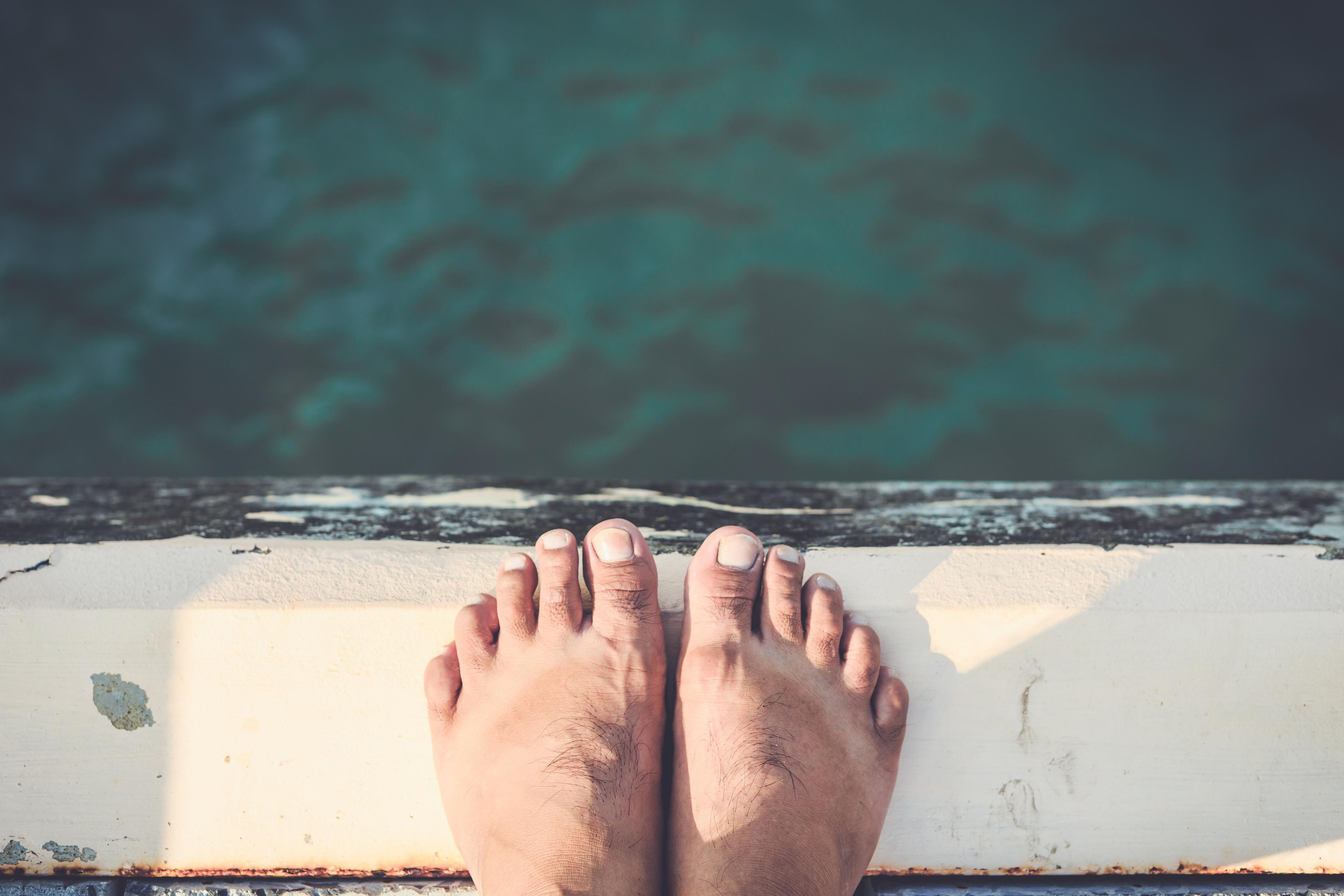 Photo of bare feet standing at the edge of a dock above green water, with a worn wooden surface beneath.
