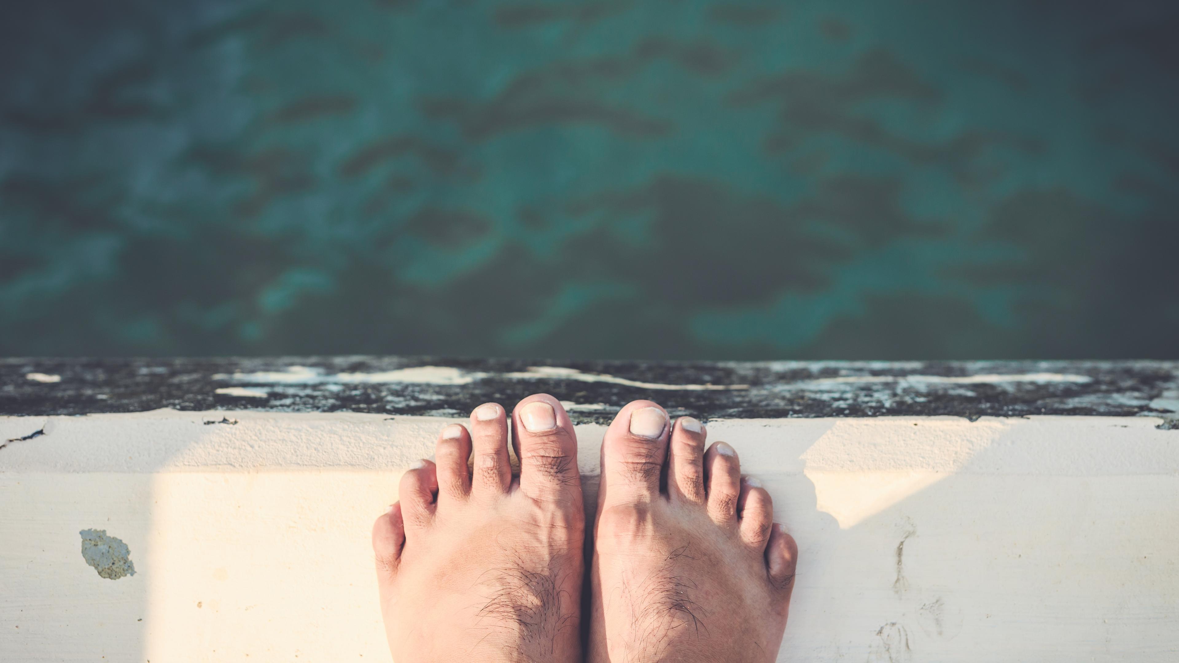 Photo of bare feet standing at the edge of a dock above green water, with a worn wooden surface beneath.