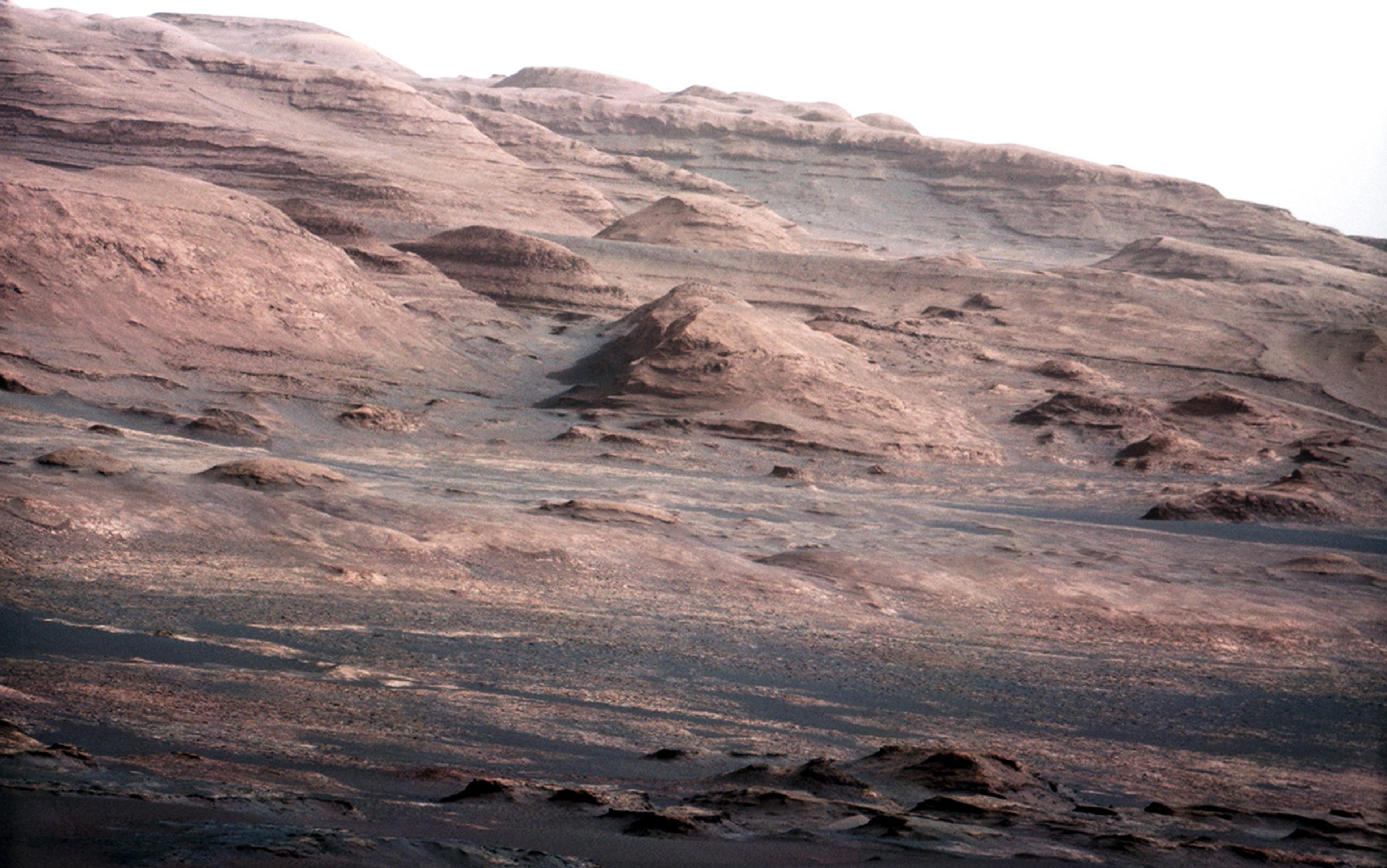 A mountainous, rocky landscape under a clear sky, featuring layered rock formations and gently sloping terrain.