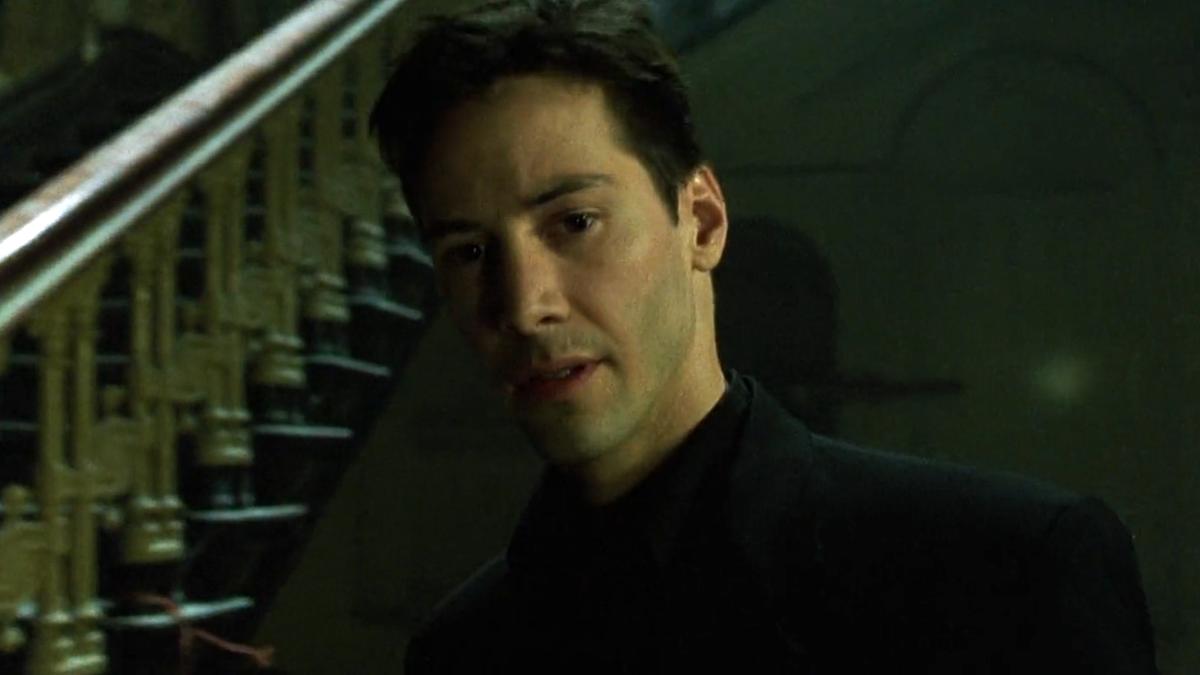Scene from a film showing a man standing indoors near a staircase bathed in green light.