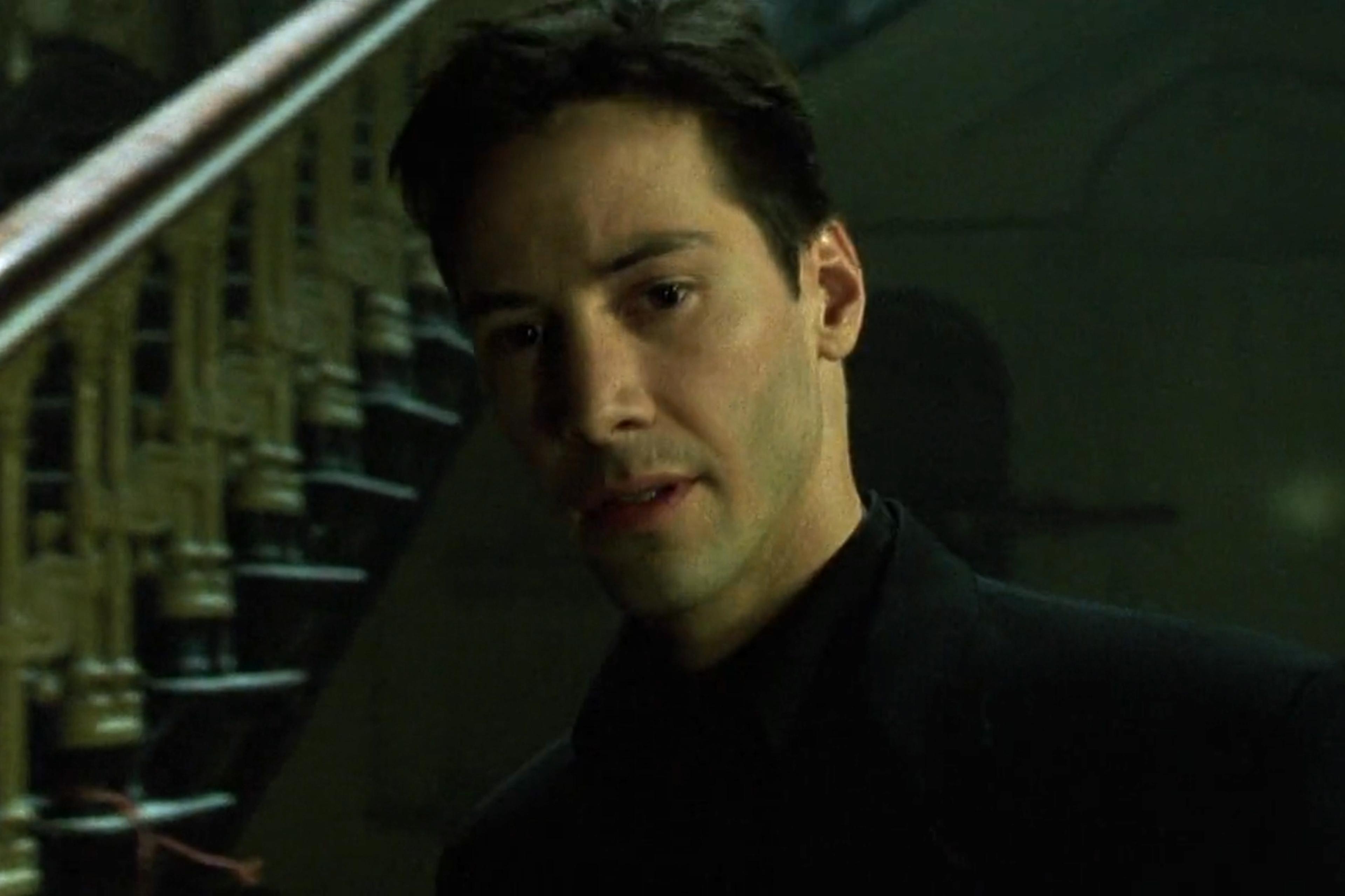 Scene from a film showing a man standing indoors near a staircase bathed in green light.