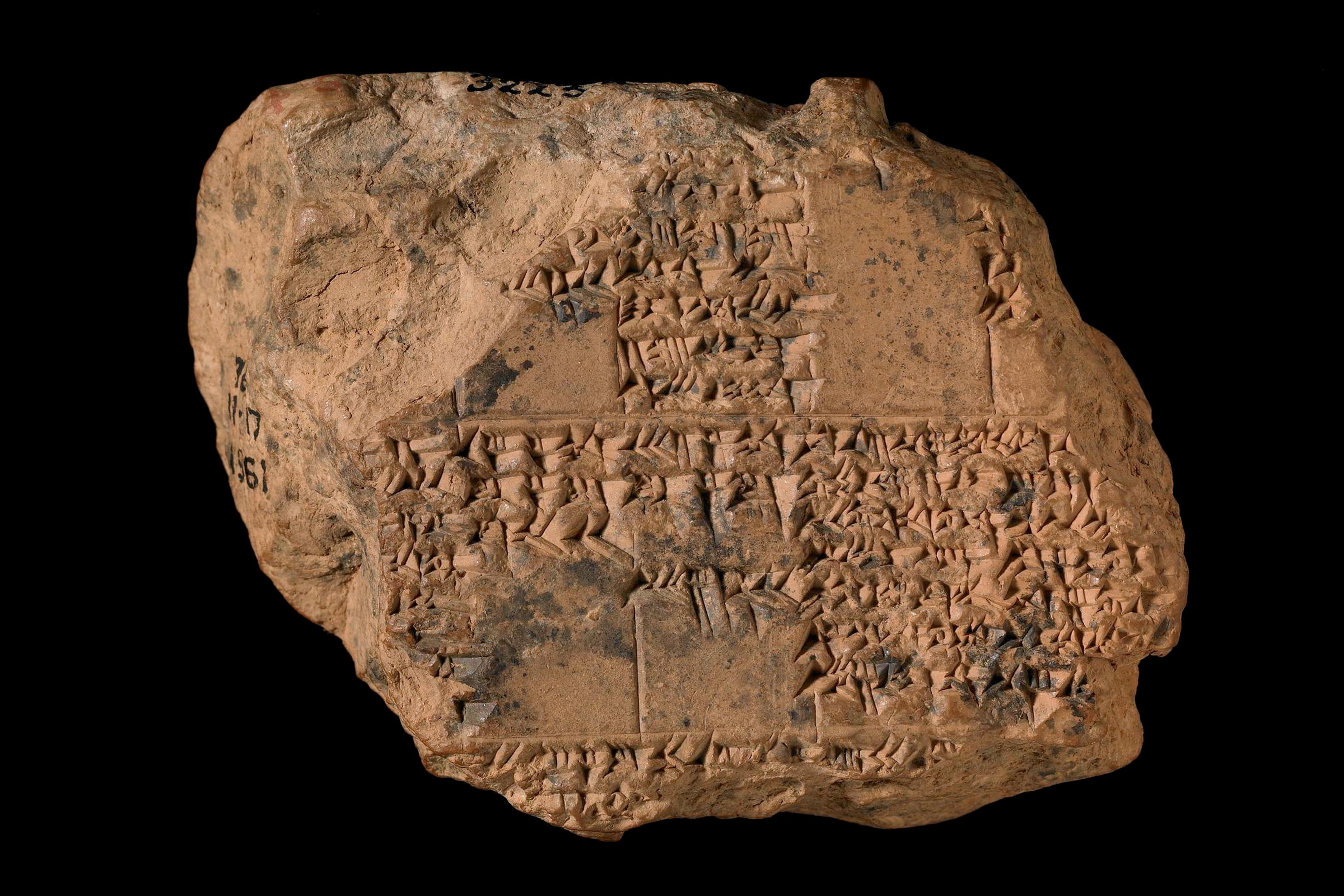 Ancient clay tablet with cuneiform script on a black background, likely an artifact from Mesopotamia.
