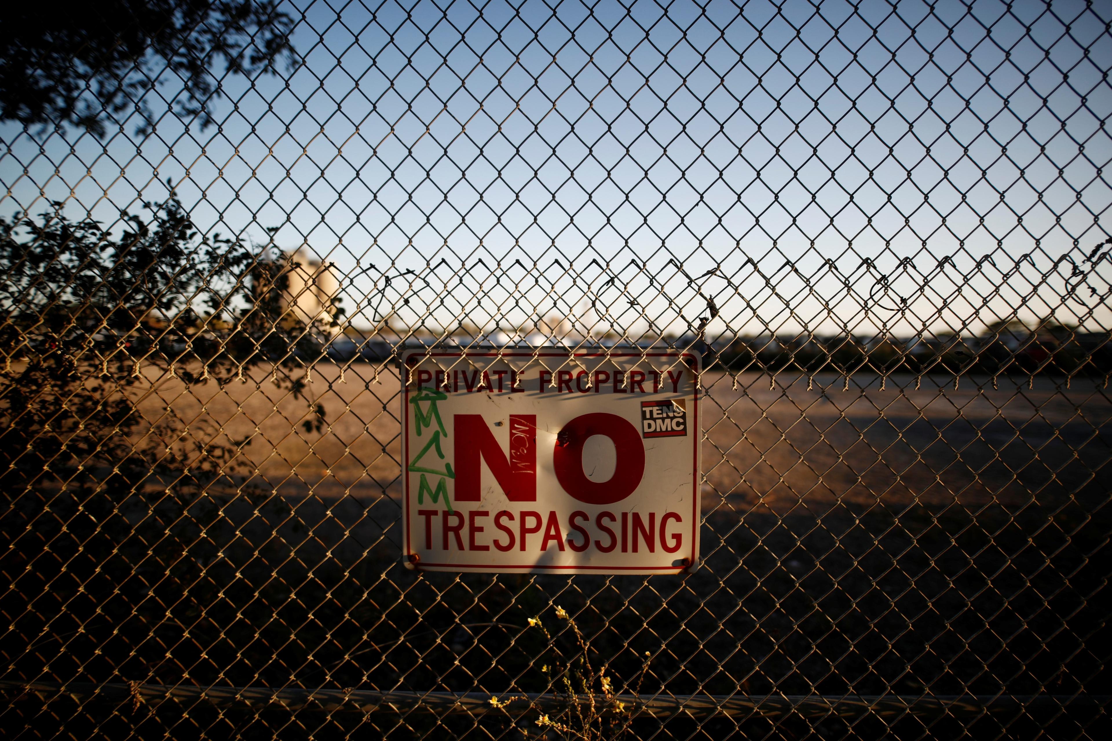 Photo of a chain-link fence with a “Private Property No Trespassing” sign in front of an open field.