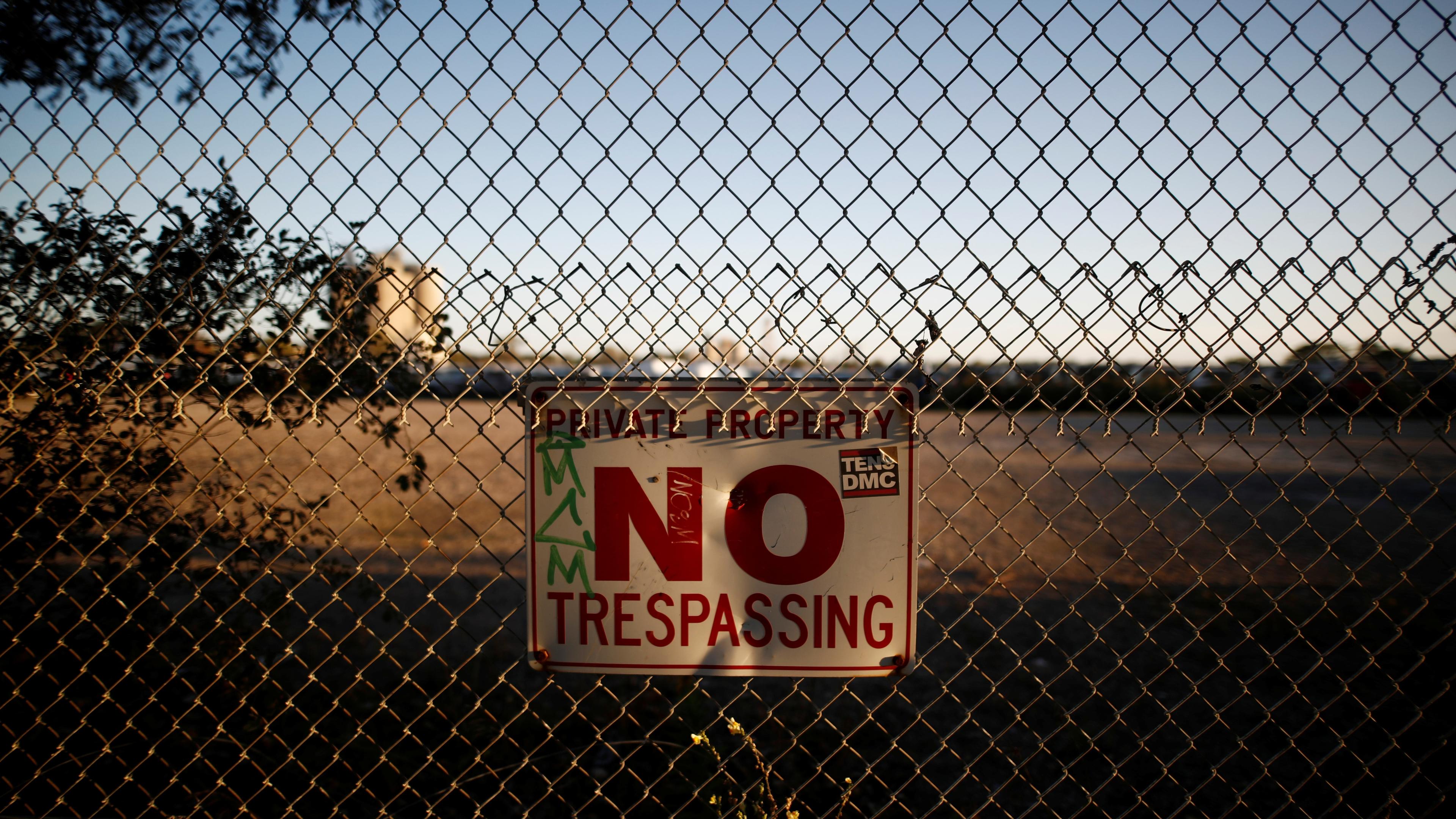 Photo of a chain-link fence with a “Private Property No Trespassing” sign in front of an open field.