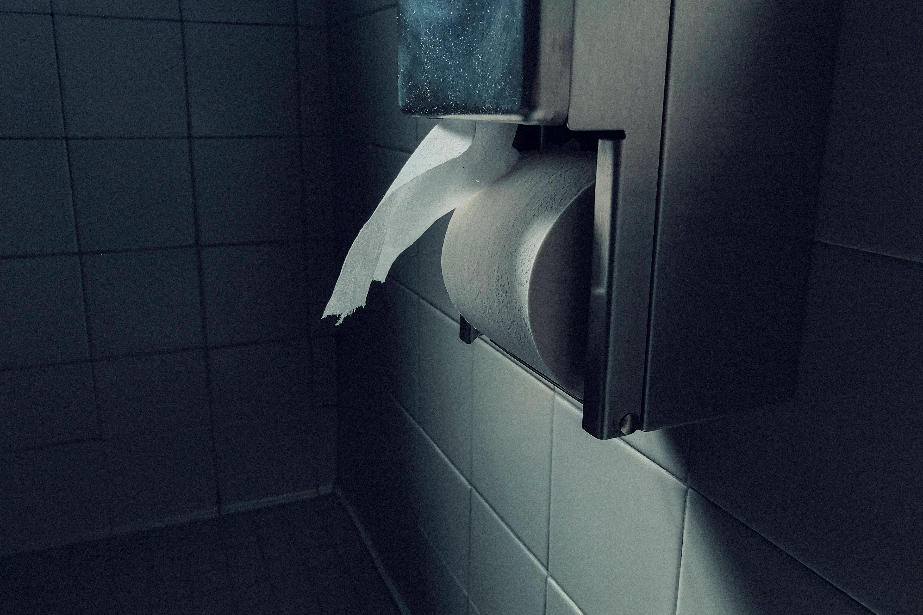 Photo of a toilet paper dispenser on a tiled wall in a dimly lit bathroom.