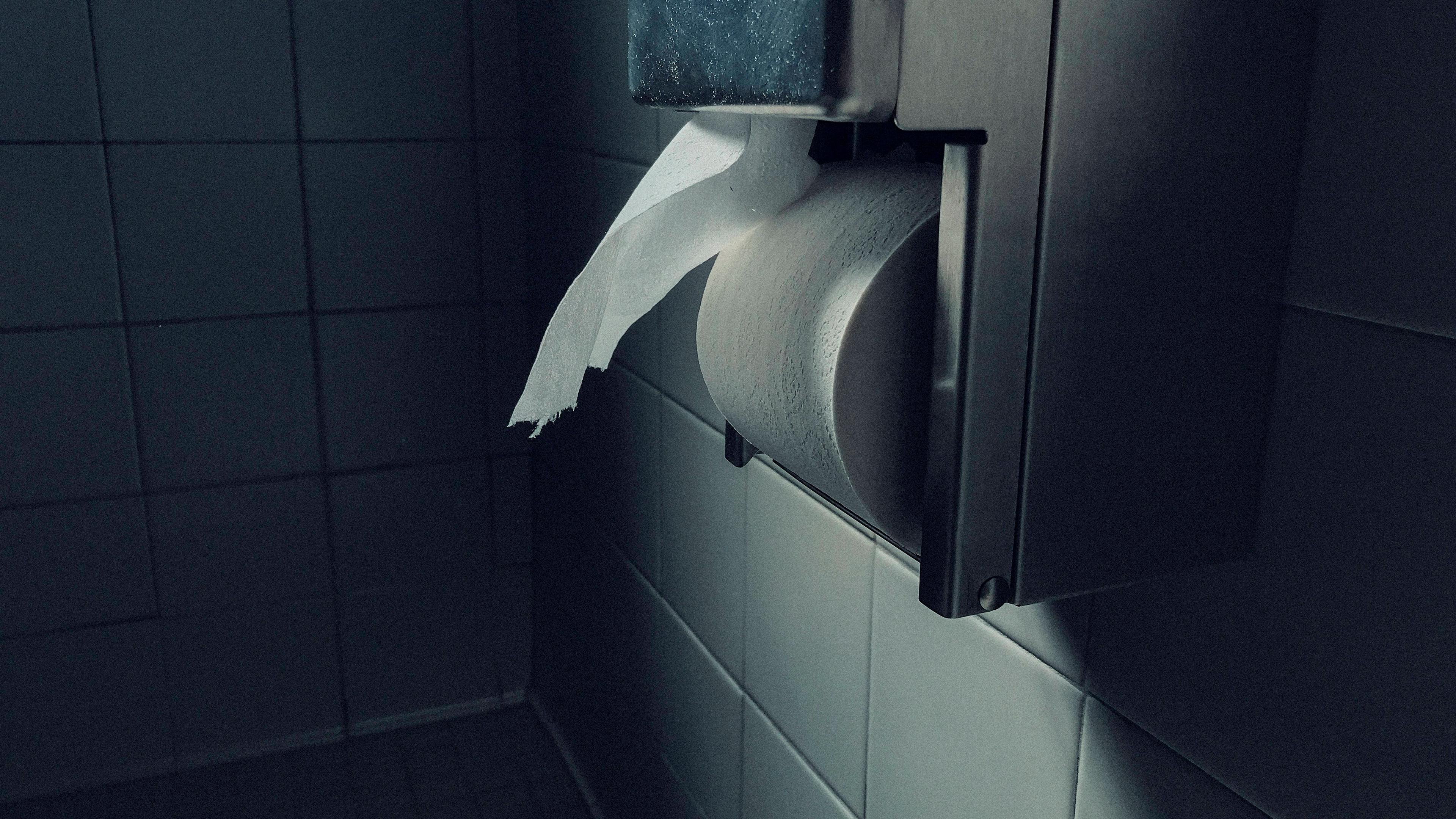 Photo of a toilet paper dispenser on a tiled wall in a dimly lit bathroom.