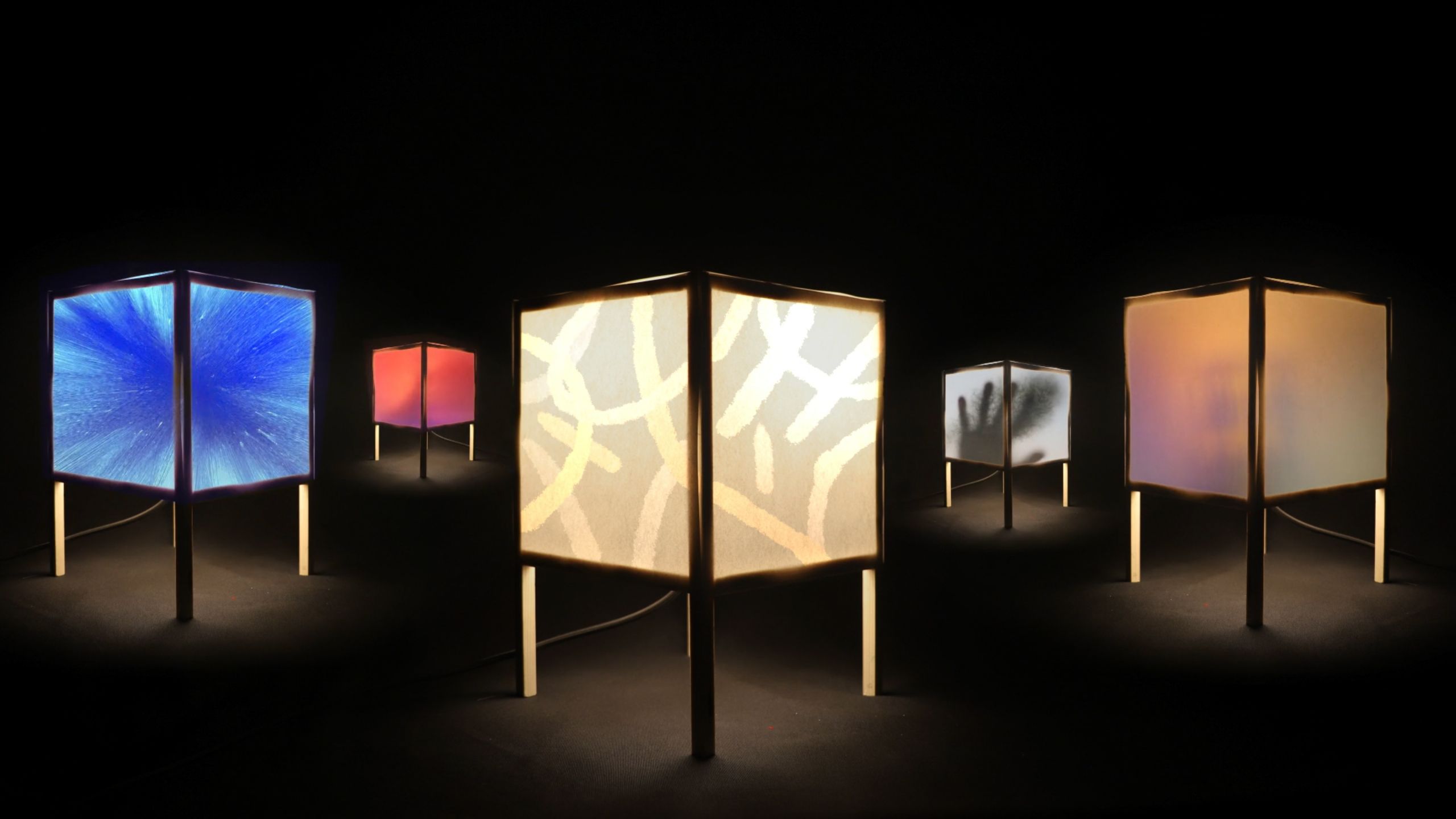Photo of six illuminated geometric lanterns with various patterns on a dark background.