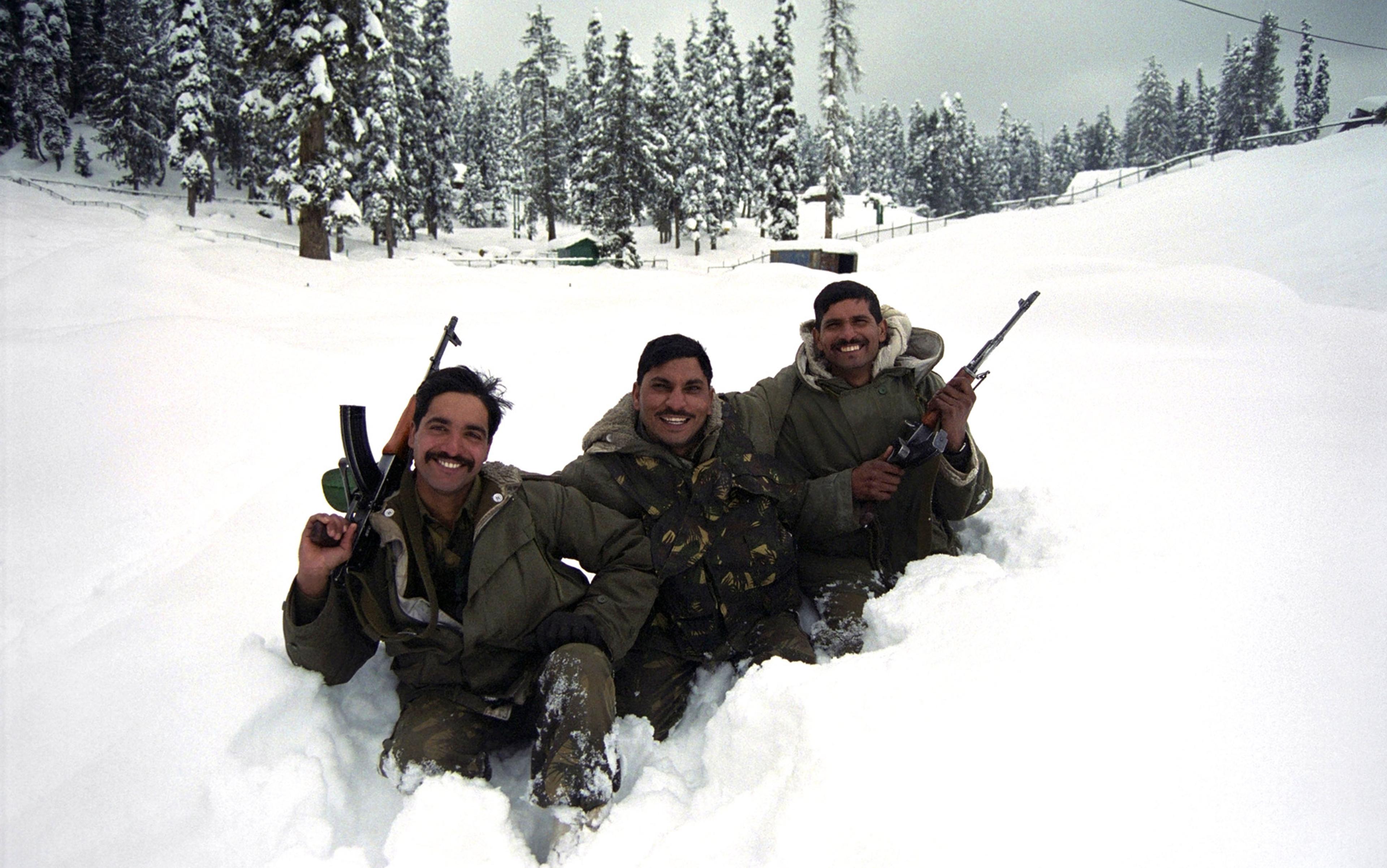 Photo of three soldiers smiling, sitting in deep snow holding rifles with a snowy forest background.