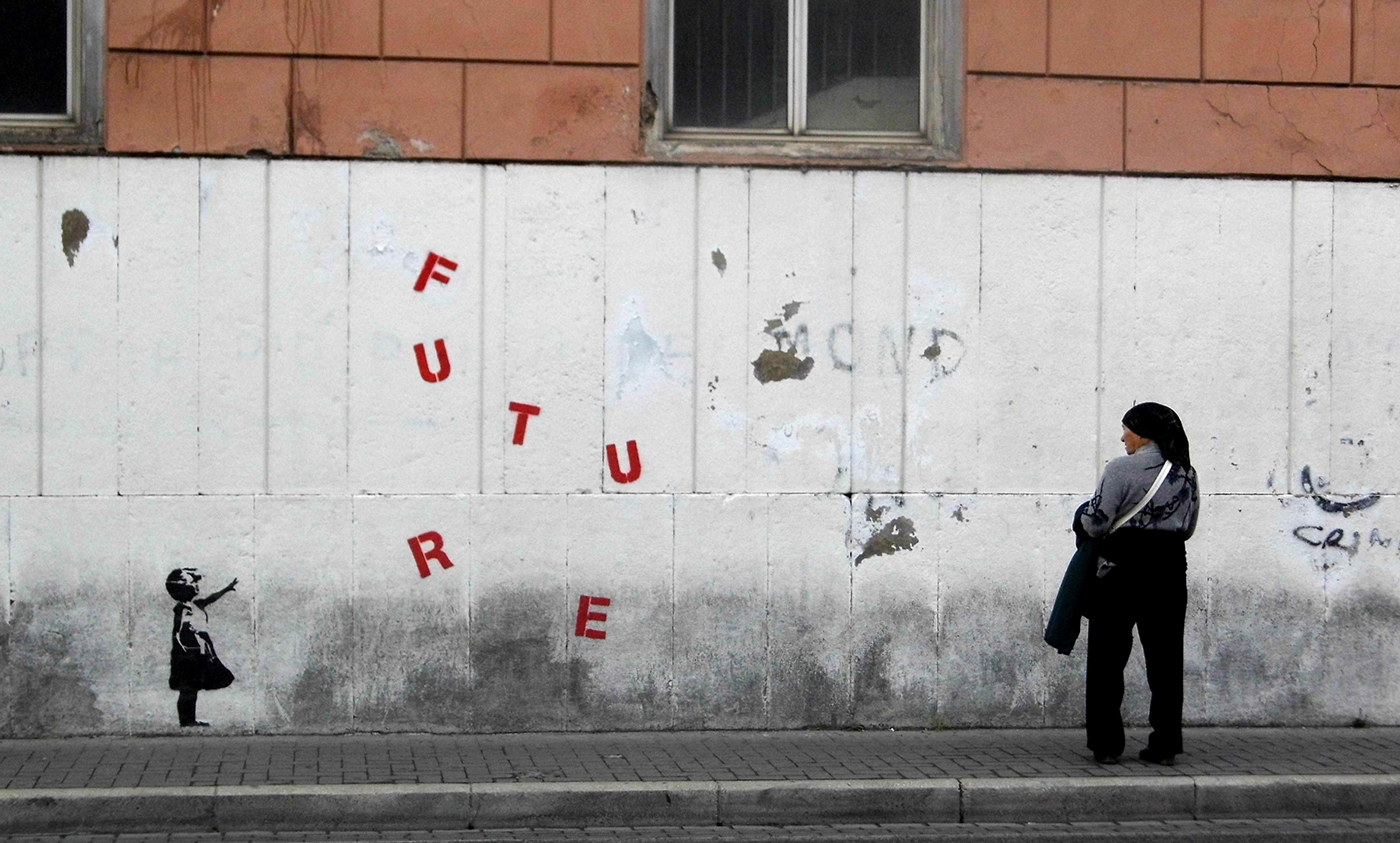 Street art depicting a child reaching for falling letters spelling ‘FUTURE’, with a woman standing nearby.