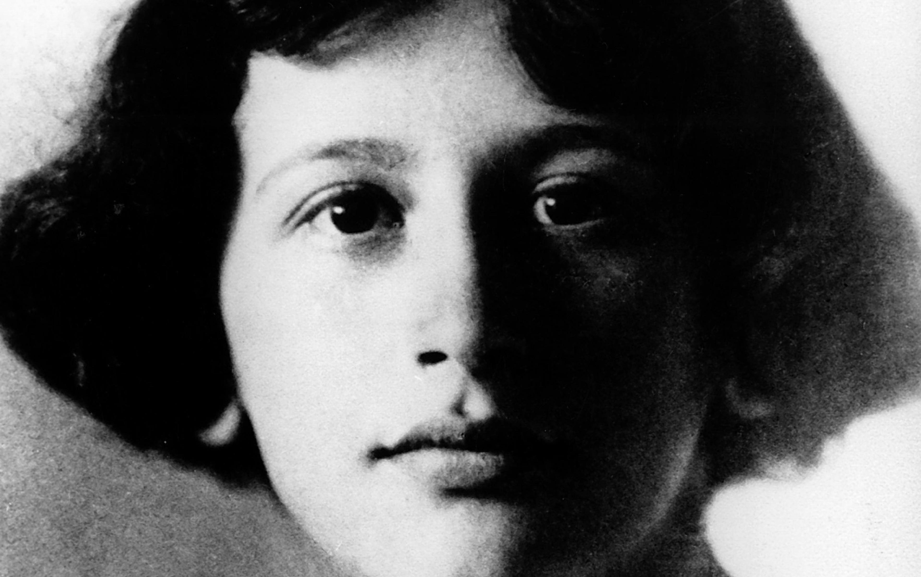 Black-and-white photo of a young woman who is Simone Weil with short hair facing the camera, half of her face in shadow.