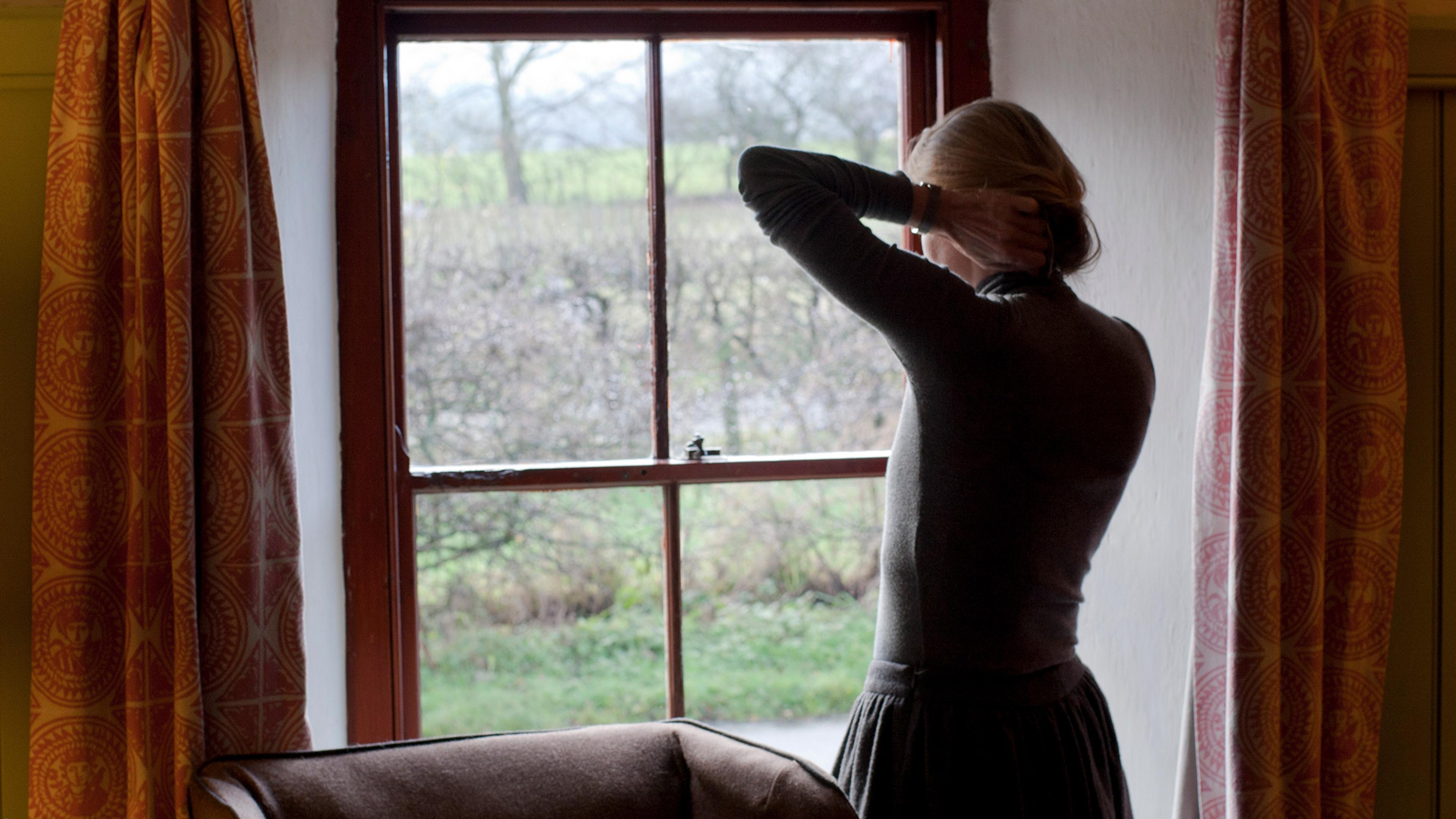 A woman seen from behind talks on a mobile phone while distractedly running her hand through her hair