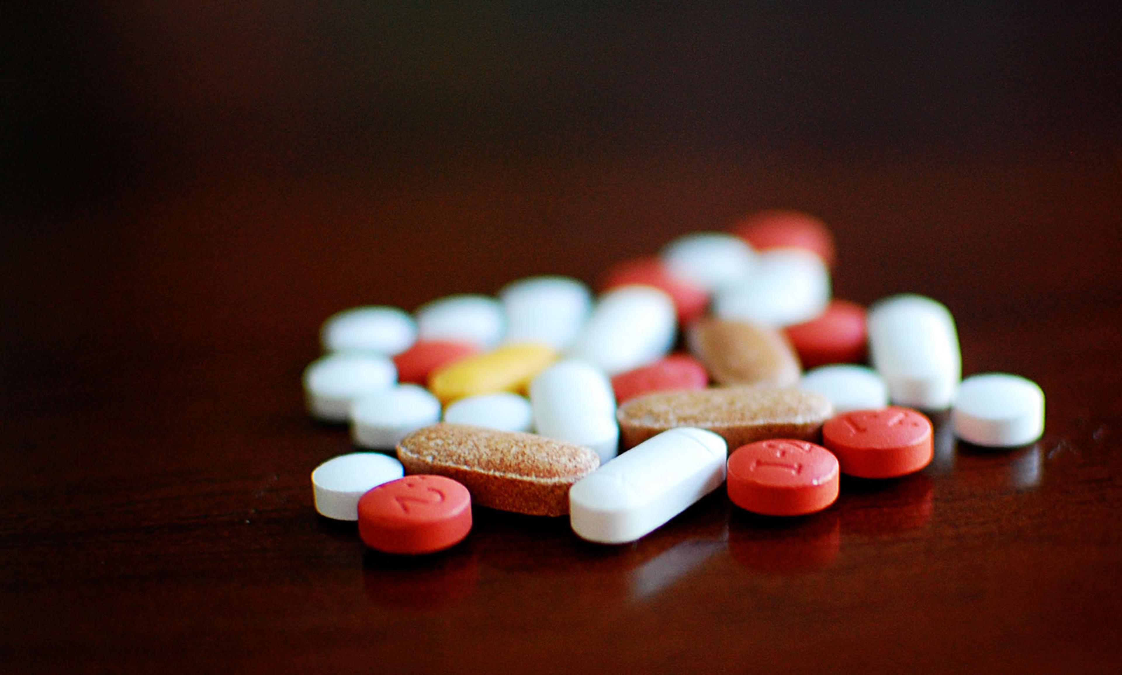 Various red, white, brown and yellow pills scattered on a dark wooden surface.