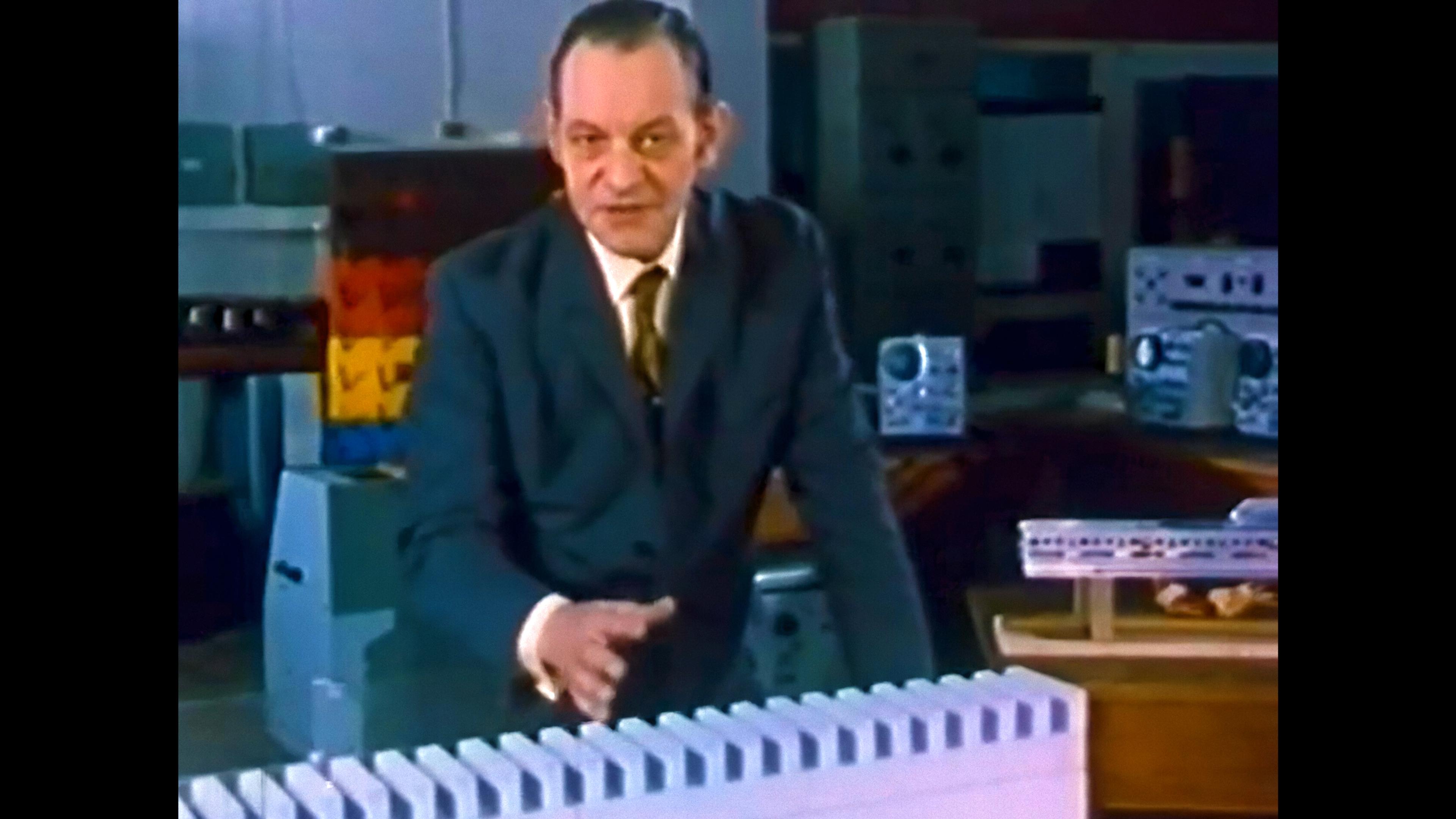 A man in a suit demonstrates with a series of blocks in a lab setting; photo.